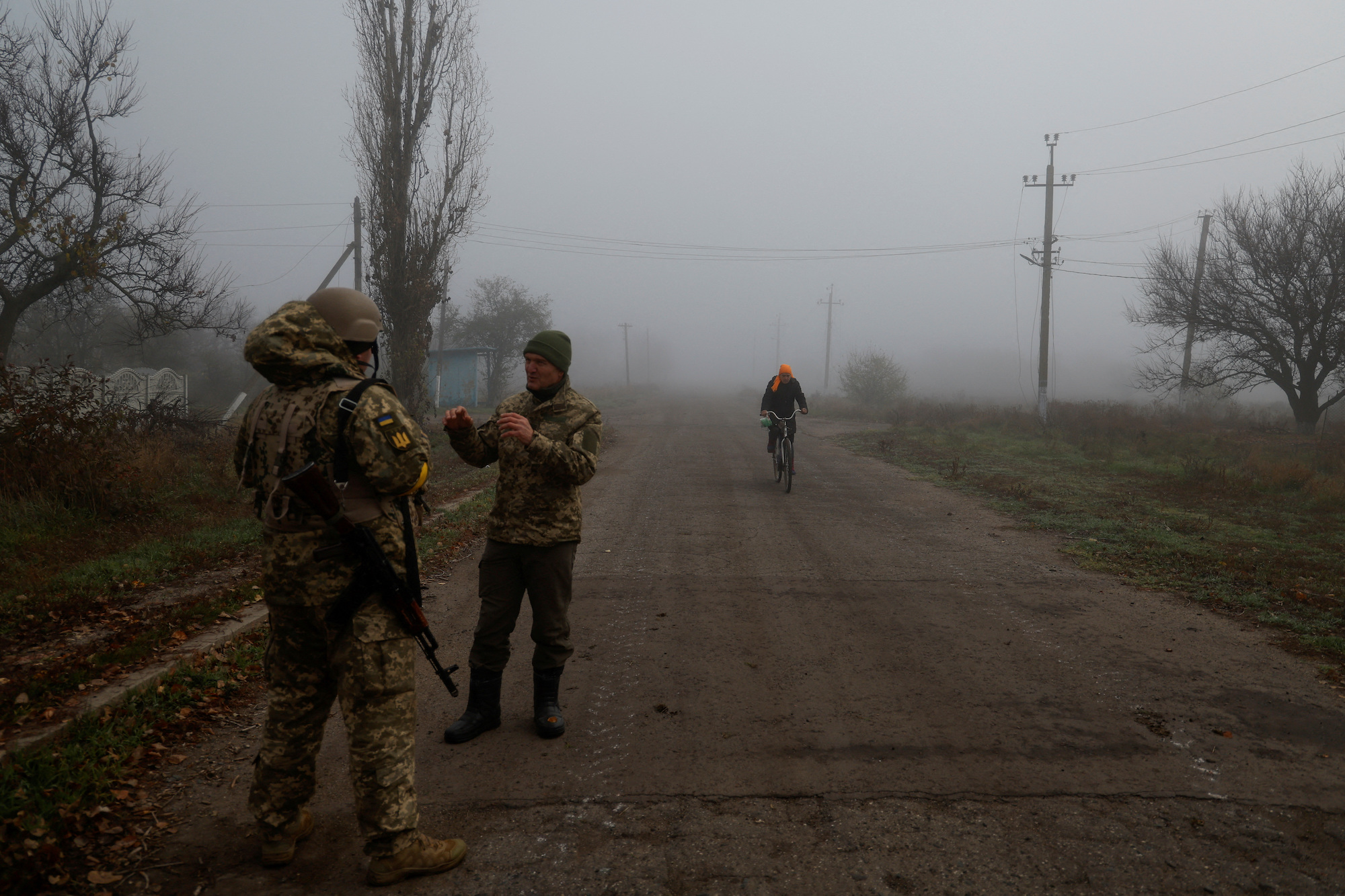 A Ukrainian serviceman speaks with a chaplain while a local resident rides a bicycle along a street, in a village near the newly recaptured city of Snihurivka, Mykolaiv region, on Thursday.
