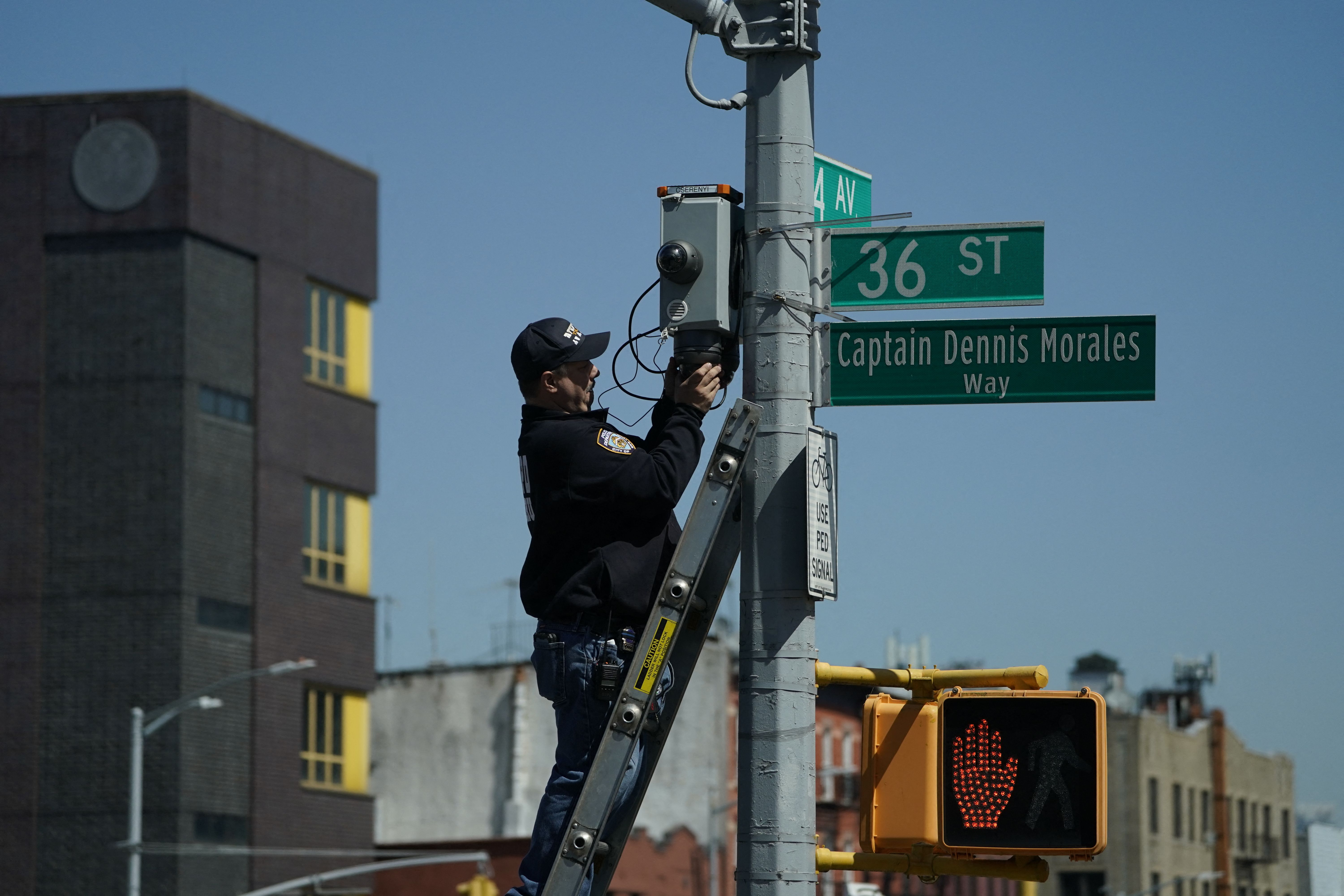 A member of the New York City Police Department climbs a ladder to retrieve a security camera near the subway station shooting in Brooklyn on Tuesday.
