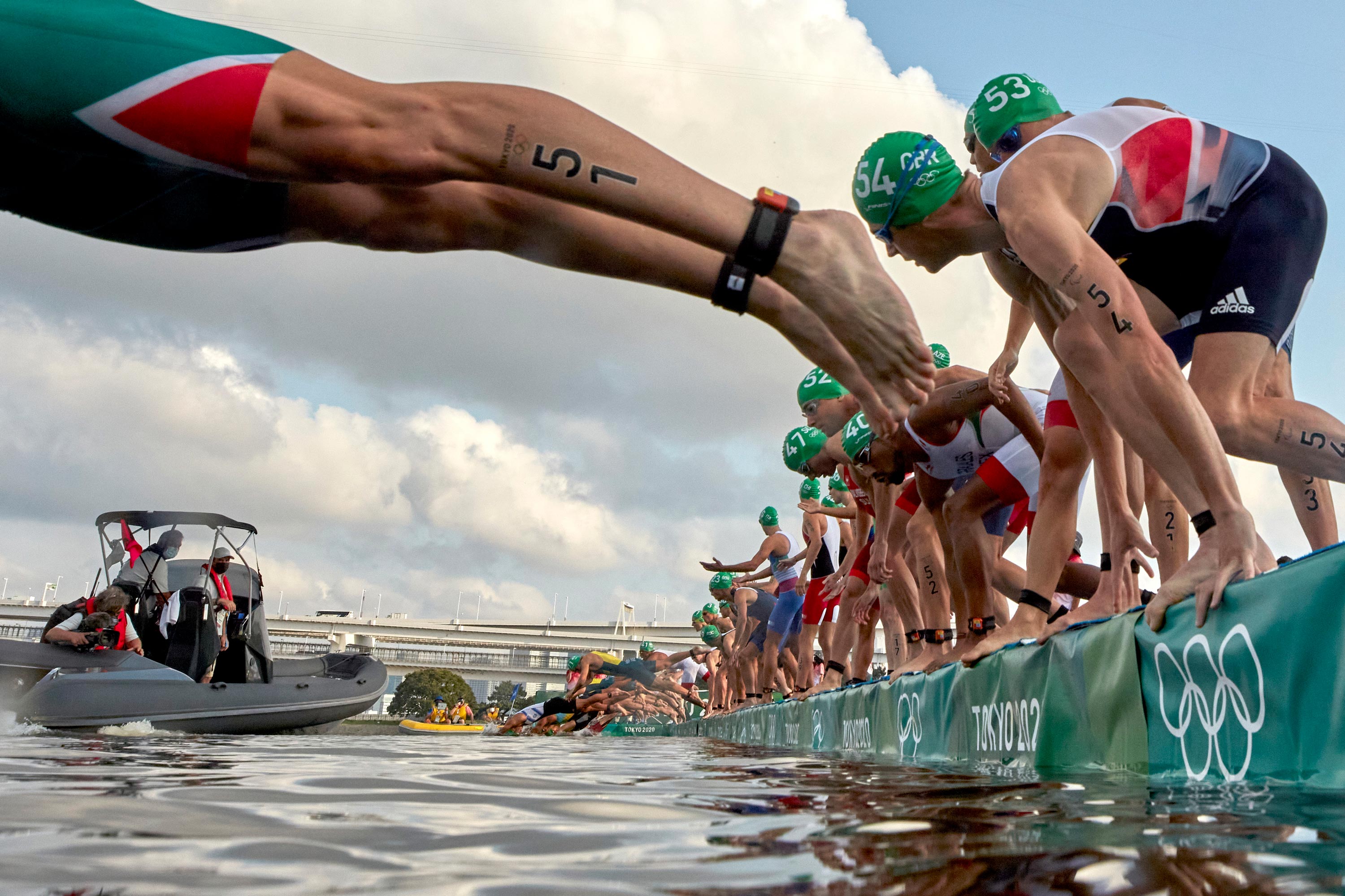 Triathletes dive into the water as a broadcast boat prevents all swimmers from starting forcing a restart before the individual triathlon on July 26.