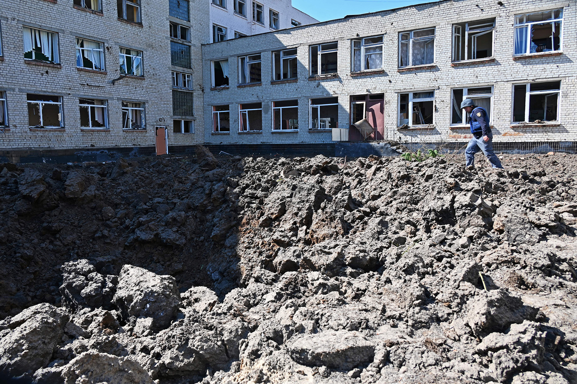 A Ukrainian deminer examines a crater caused by missile strikes that struck the yard of a school in a residential area of Kharkiv, Ukraine, on June 27.