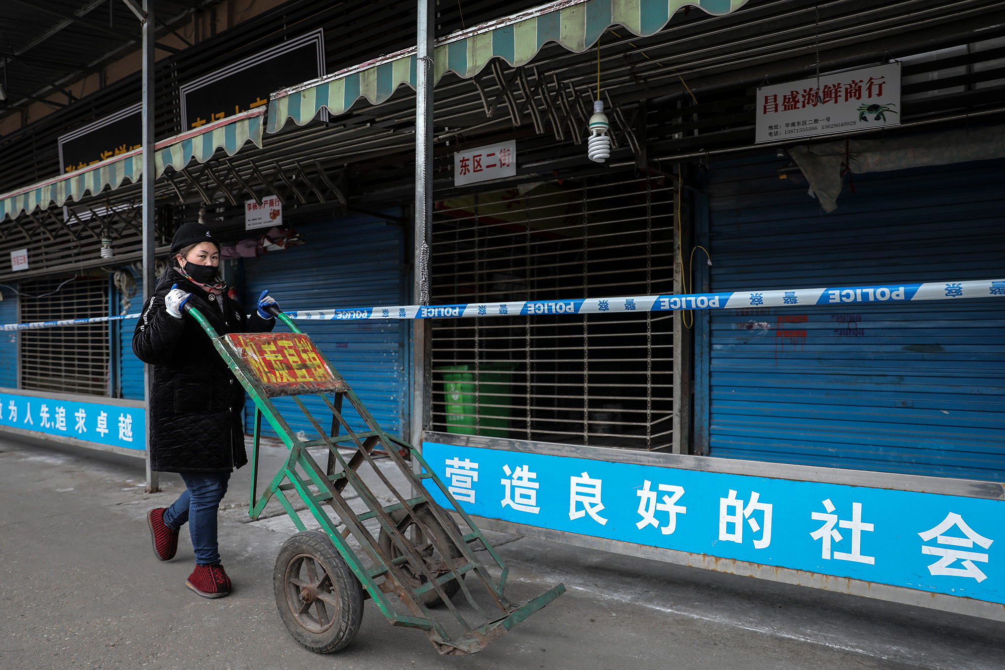 A woman wears a mask while pushing a wheelbarrow past the closed Huanan Seafood Wholesale Market. 