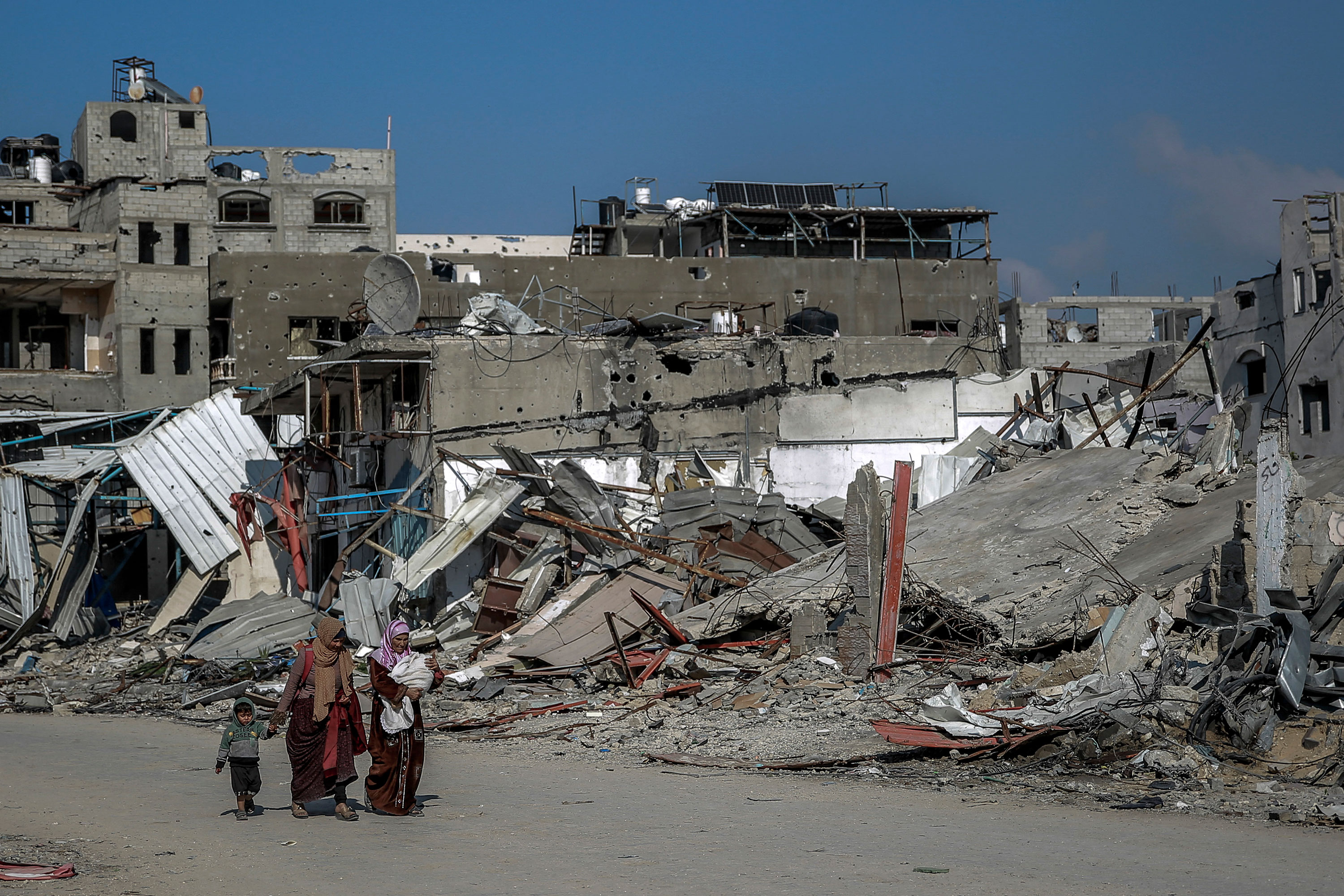 נשים וילדים פלסטיניים חולפים על פני בניינים שנהרסו במהלך התקיפות הישראליות בבית לאהיה, עזה, ב-26 בפברואר. 