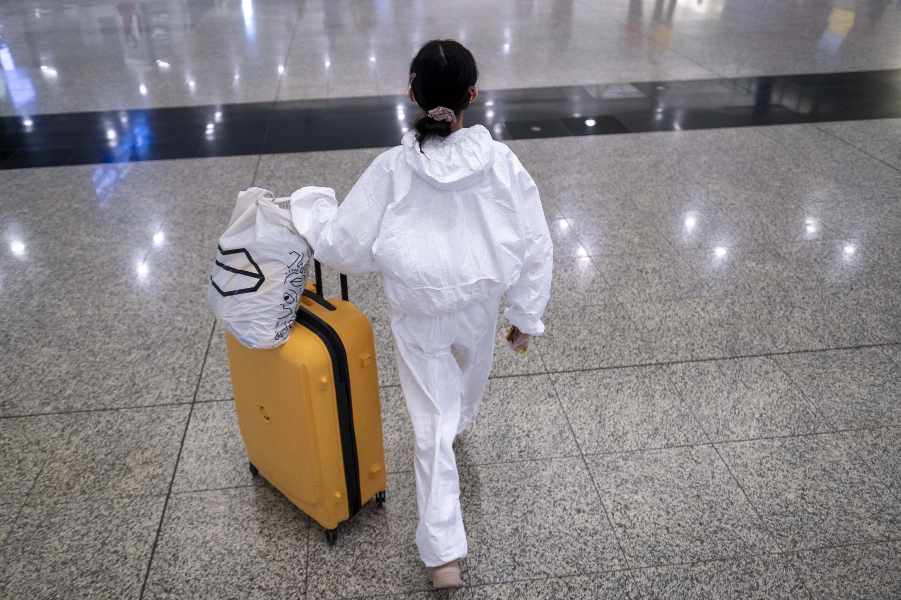A traveler wearing a protective suit walks with luggage through the arrivals hall of Hong Kong International Airport on March 18.