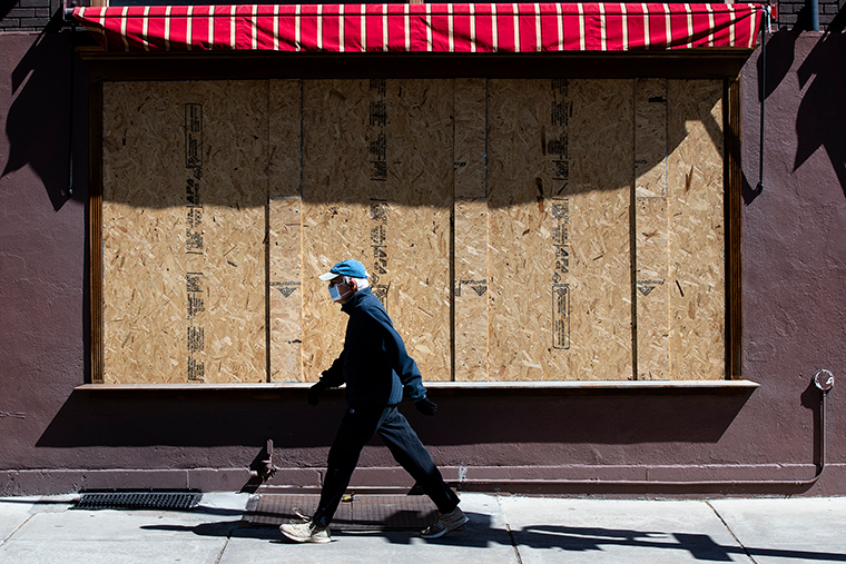 A person wearing a mask walks past a boarded up business in Philadelphia, on Thursday, April 2. (