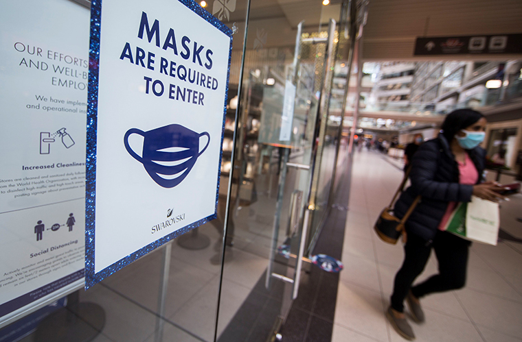 A woman wearing a face mask walks past a store with a notice of mandatory mask requirement at CF Toronto Eaton Center in Toronto, Canada, on Oct. 6, 2020. 