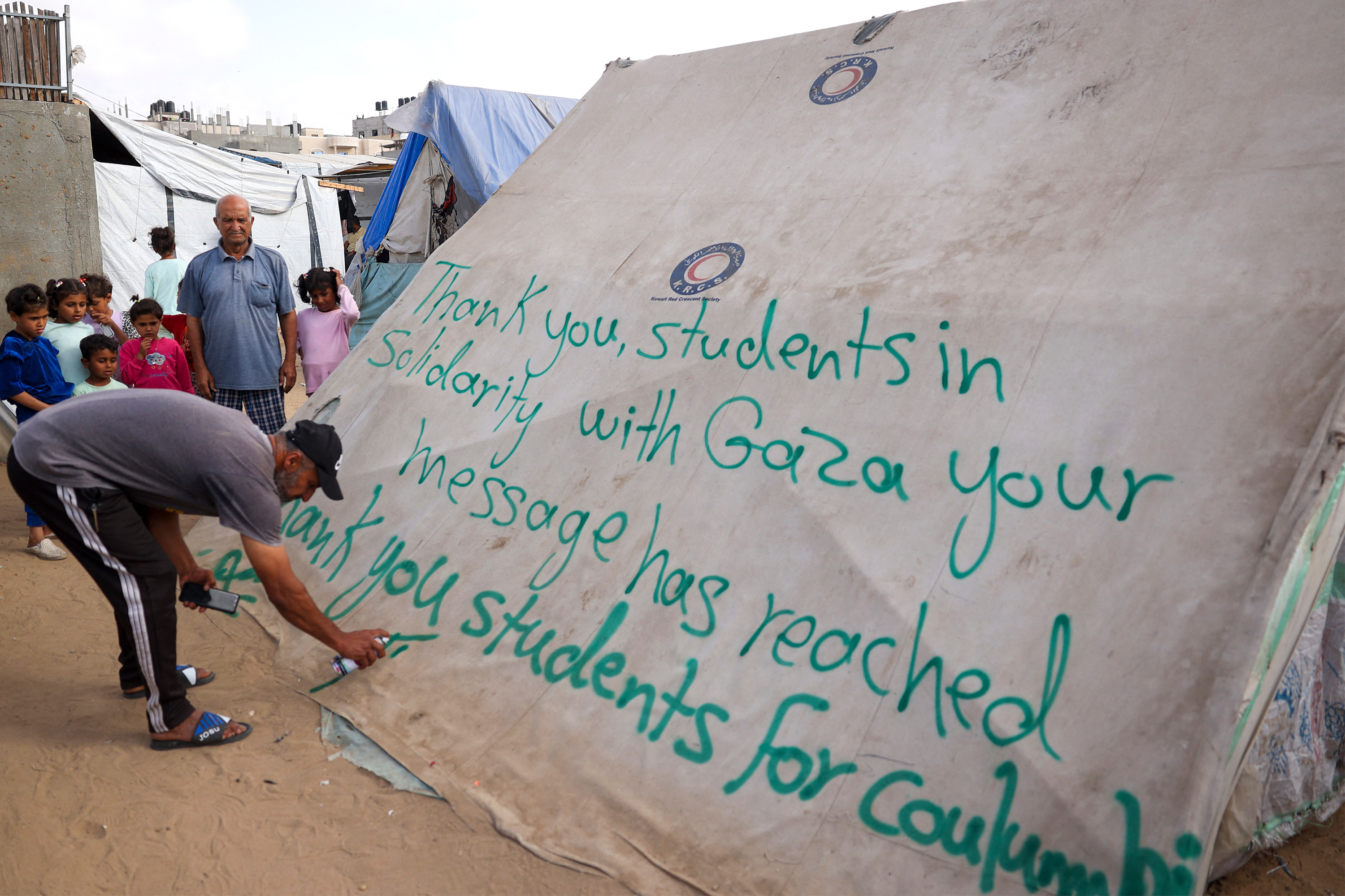 A man writes a message of thanks to students in the US protesting in solidarity with the people of Gaza, on a tent at a camp for displaced Palestinians in Rafah, Gaza, on April 27. 