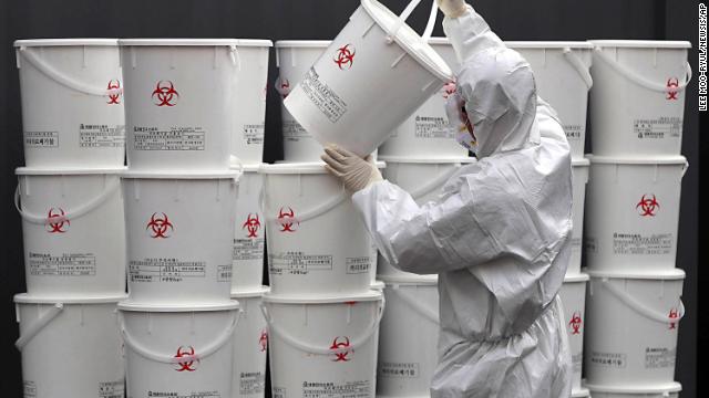 A worker in protective gear stacks plastic buckets containing medical waste from coronavirus patients at a medical center in Daegu, South Korea.