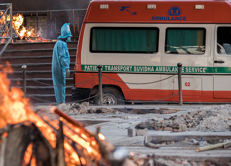 A man wearing PPE suit waits to transfer the body of his relative who died of the Covid-19 coronavirus infection from an ambulance amid burning pyres of other covid deaths at a crematorium on April 17, 2021 in New Delhi, India.