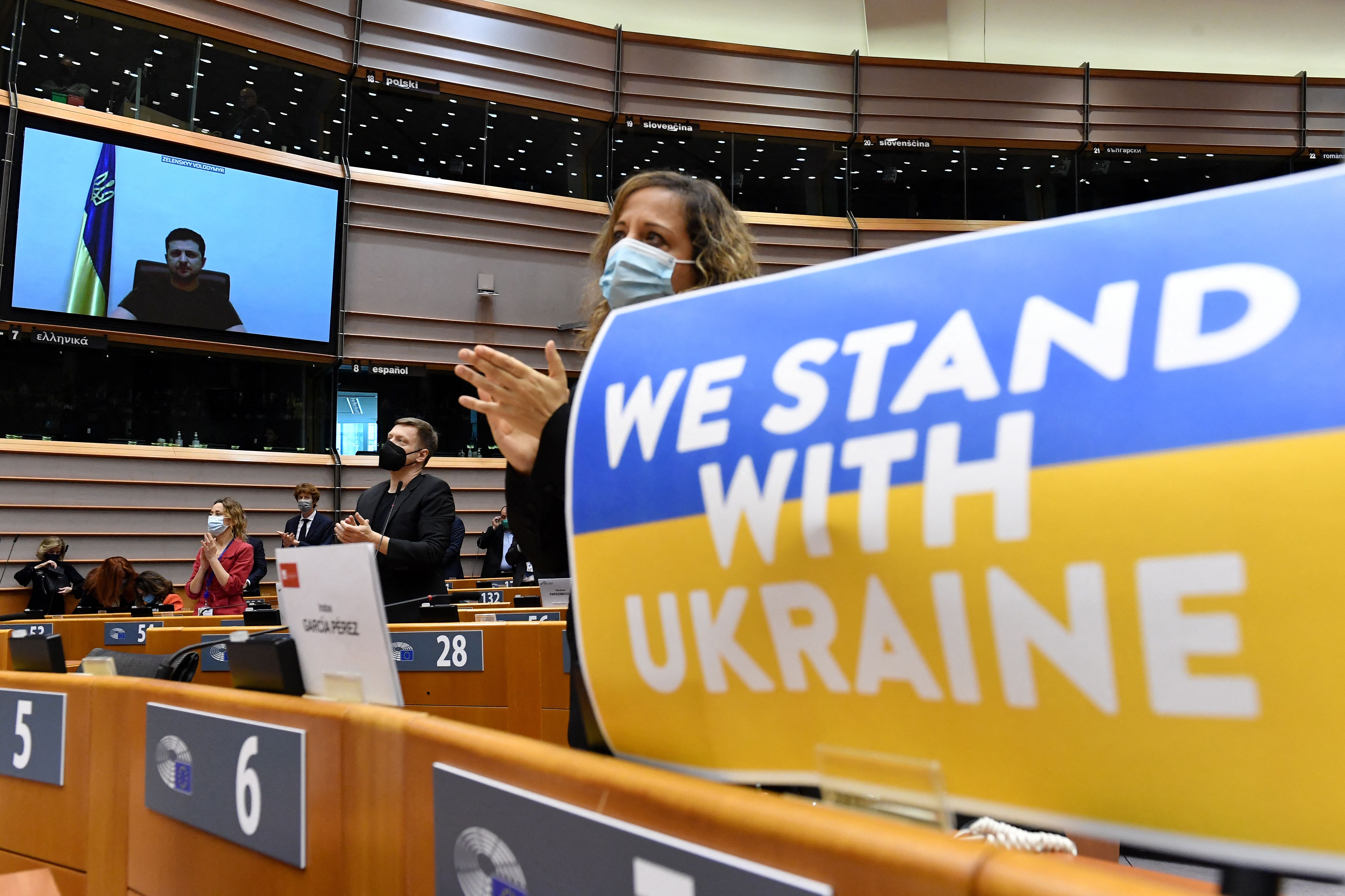 Members of the European Parliament applaud Ukrainian President Volodymyr Zelensky who appears on a screen as he speaks in a video conference during a special plenary session of the European Parliament focused on the Russian invasion of Ukraine at the EU headquarters in Brussels, on March 1.