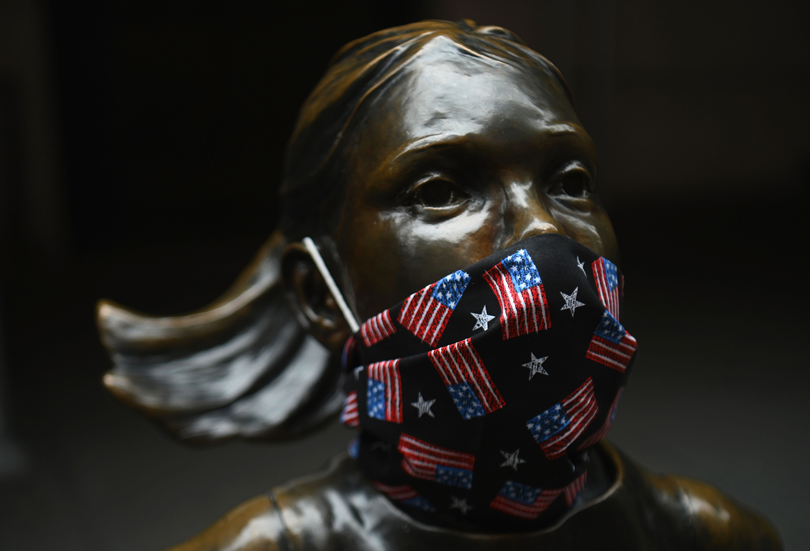 The "Fearless Girl" statue wears a face mask with American Flags outside the New York Stock Exchange at Wall Street on April 23, in New York City.
