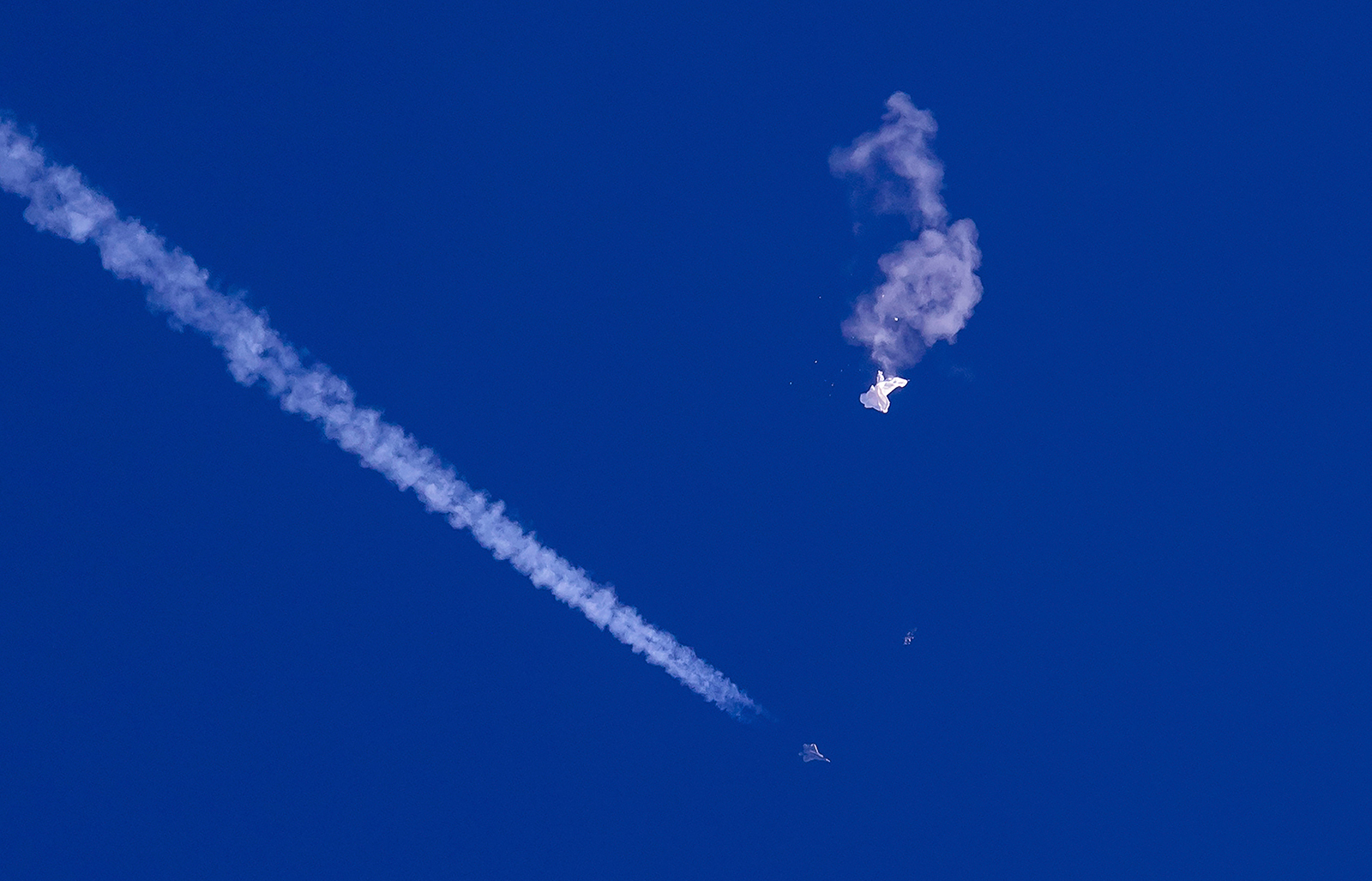 In this photo provided by Chad Fish, the remnants of a large balloon drift above the Atlantic Ocean, just off the coast of South Carolina, with a fighter jet and its contrail seen below it, on February 4.