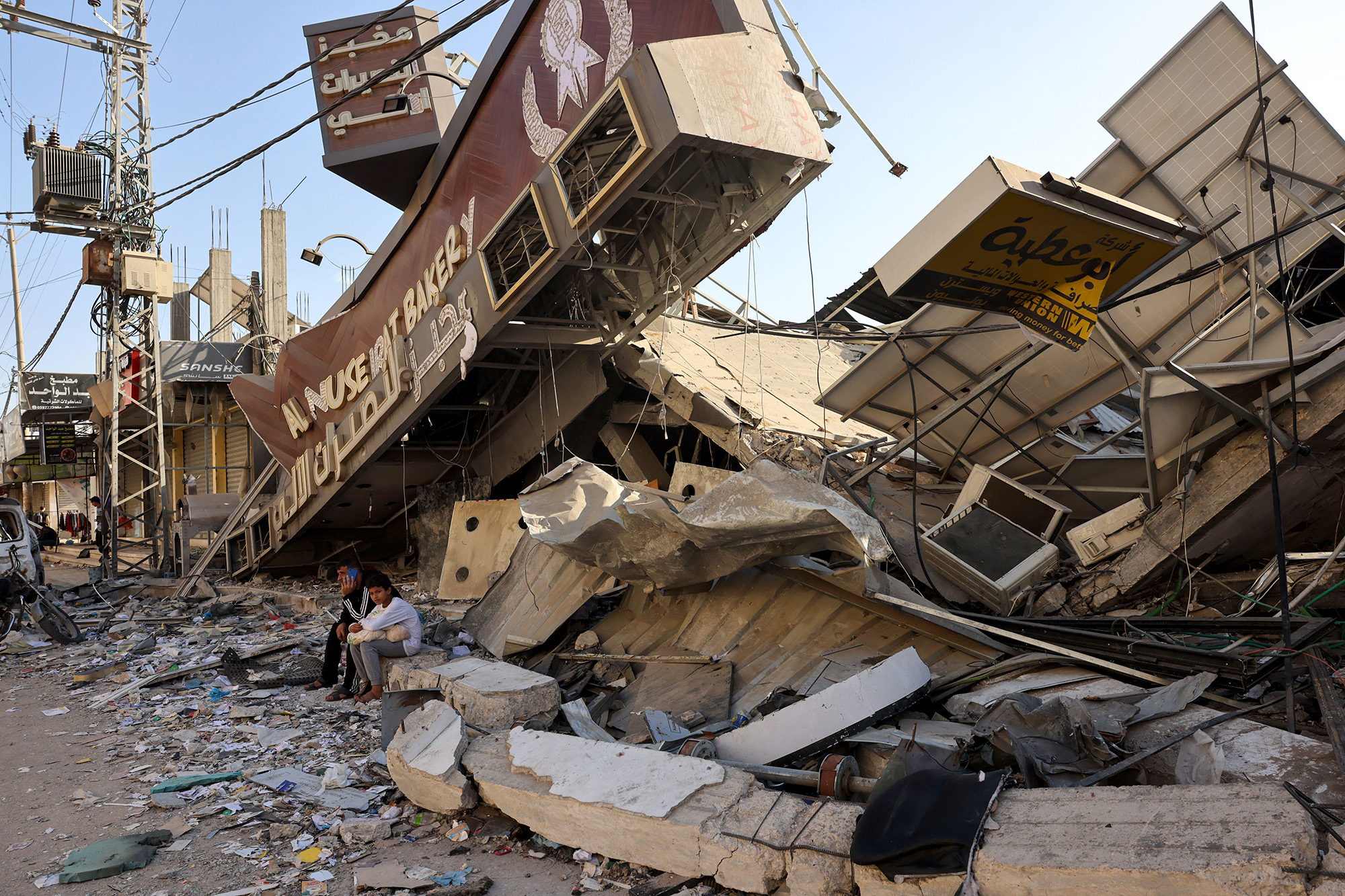 A Palestinian man and his son sit holding a bag of bread outside a destroyed bakery at the Nuseirat refugee camp in central Gaza on November 4.