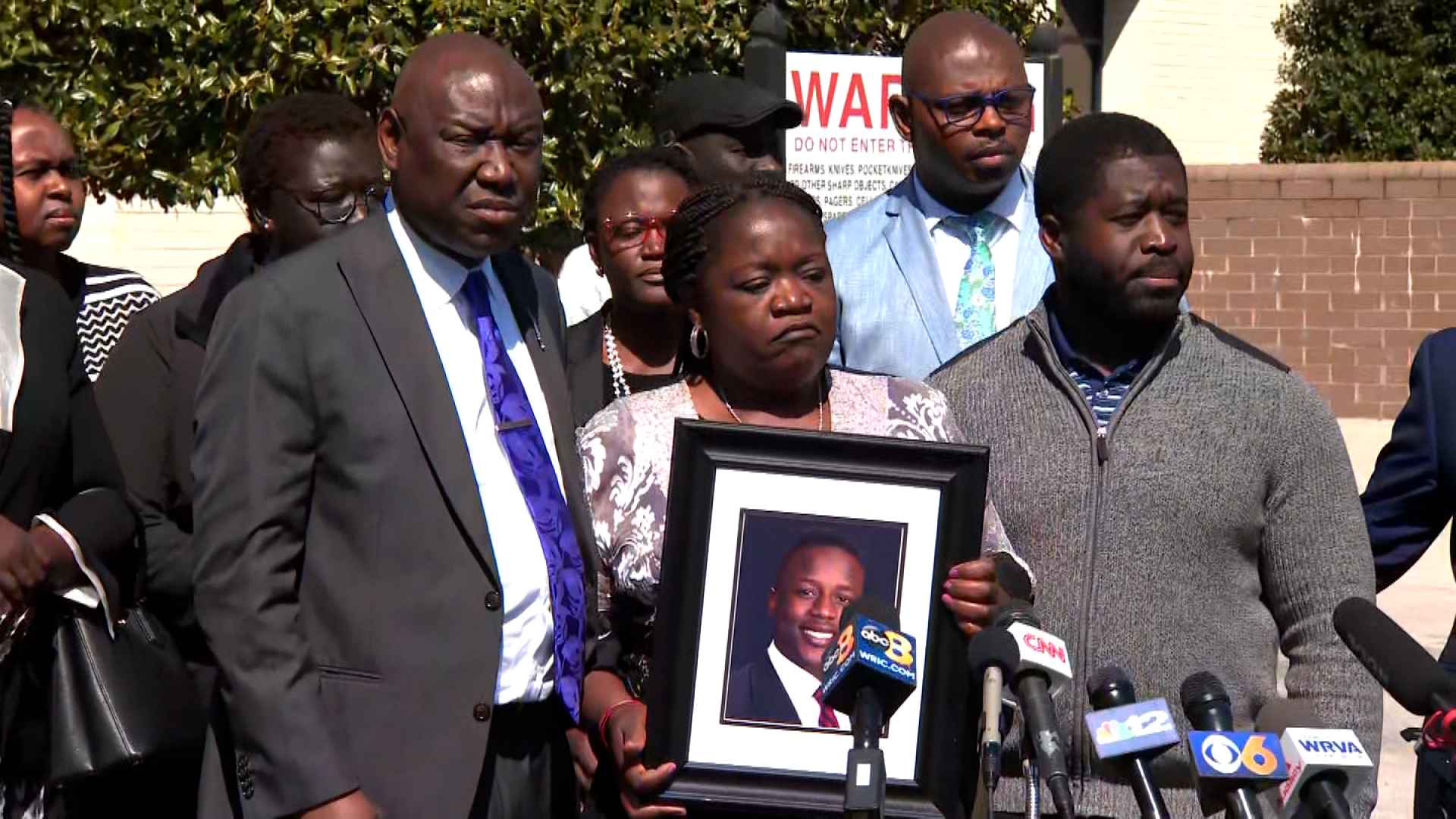 Caroline Ouko holds a portrait of her son alongside attorney Ben Crump, left, and her other son, Leon Ochieng, right, during a press conference on March 16 in Dinwiddie, Virginia. 