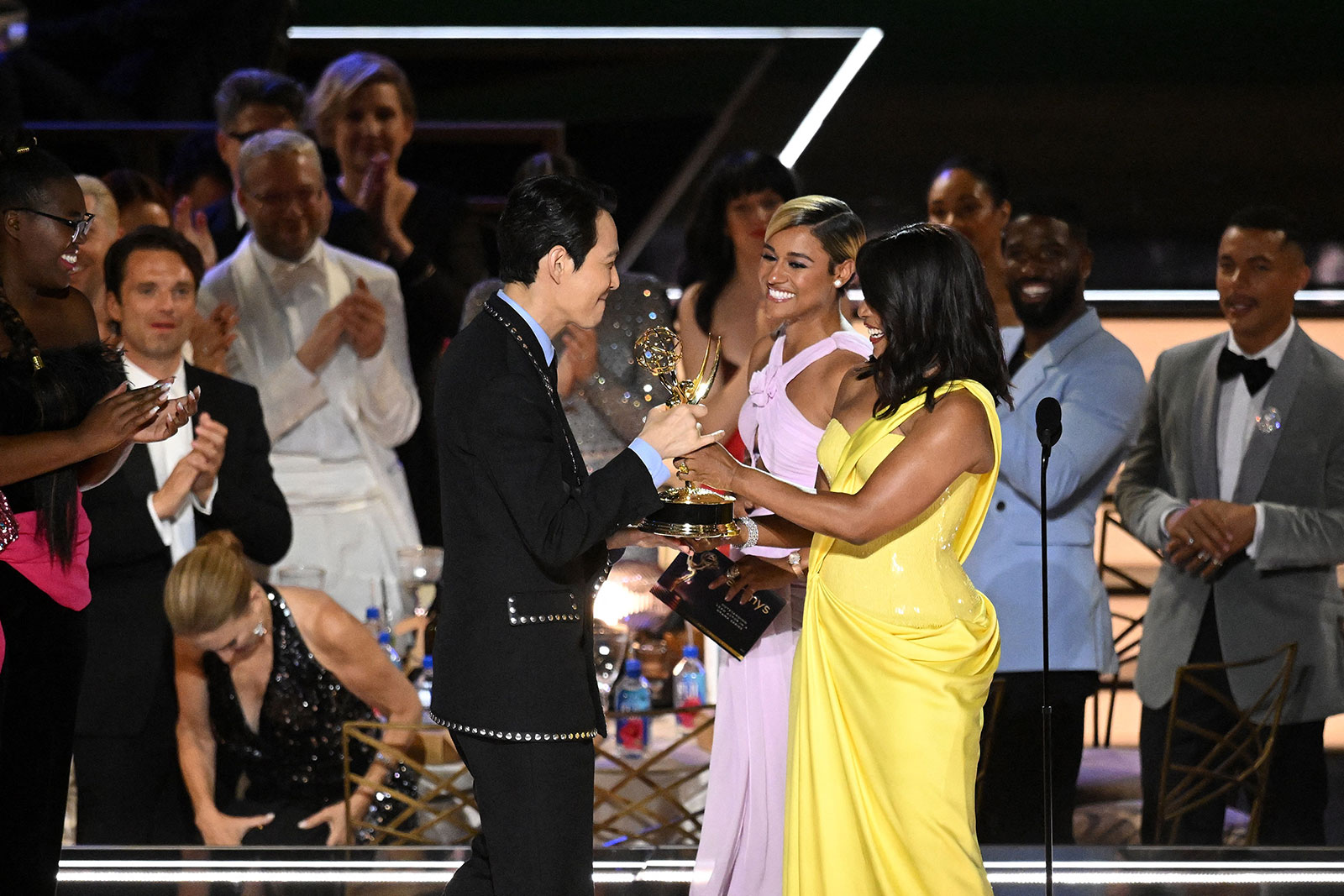 South Korean actor Lee Jung-jae, left, accepts the Emmy for outstanding lead actor in a drama series from Ariana DeBose, second from right, and Angela Bassett.