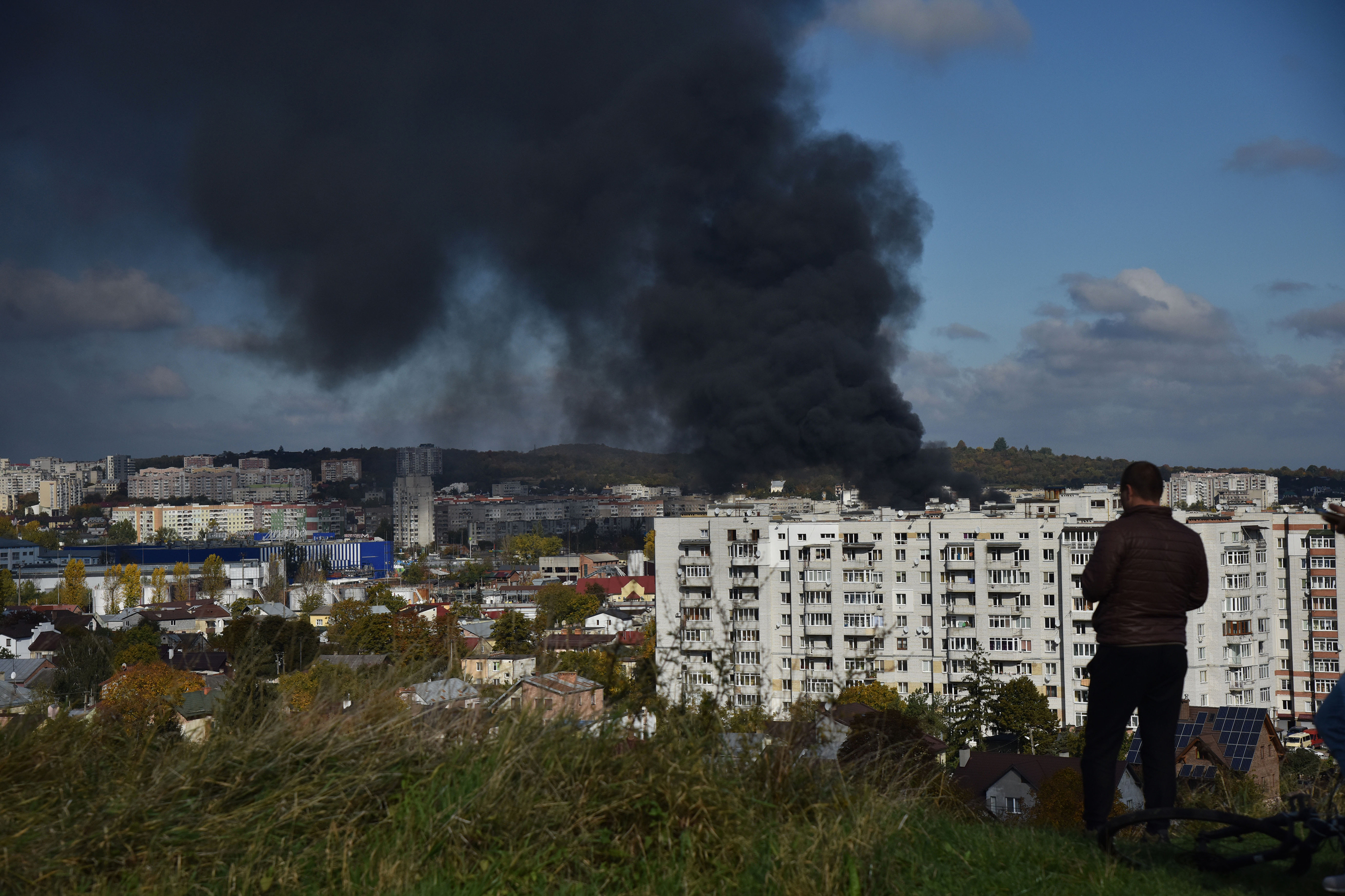 A man watches as smoke rises above the buildings after the Russian missile attack on the critical infrastructure of Lviv on Monday, October 10.