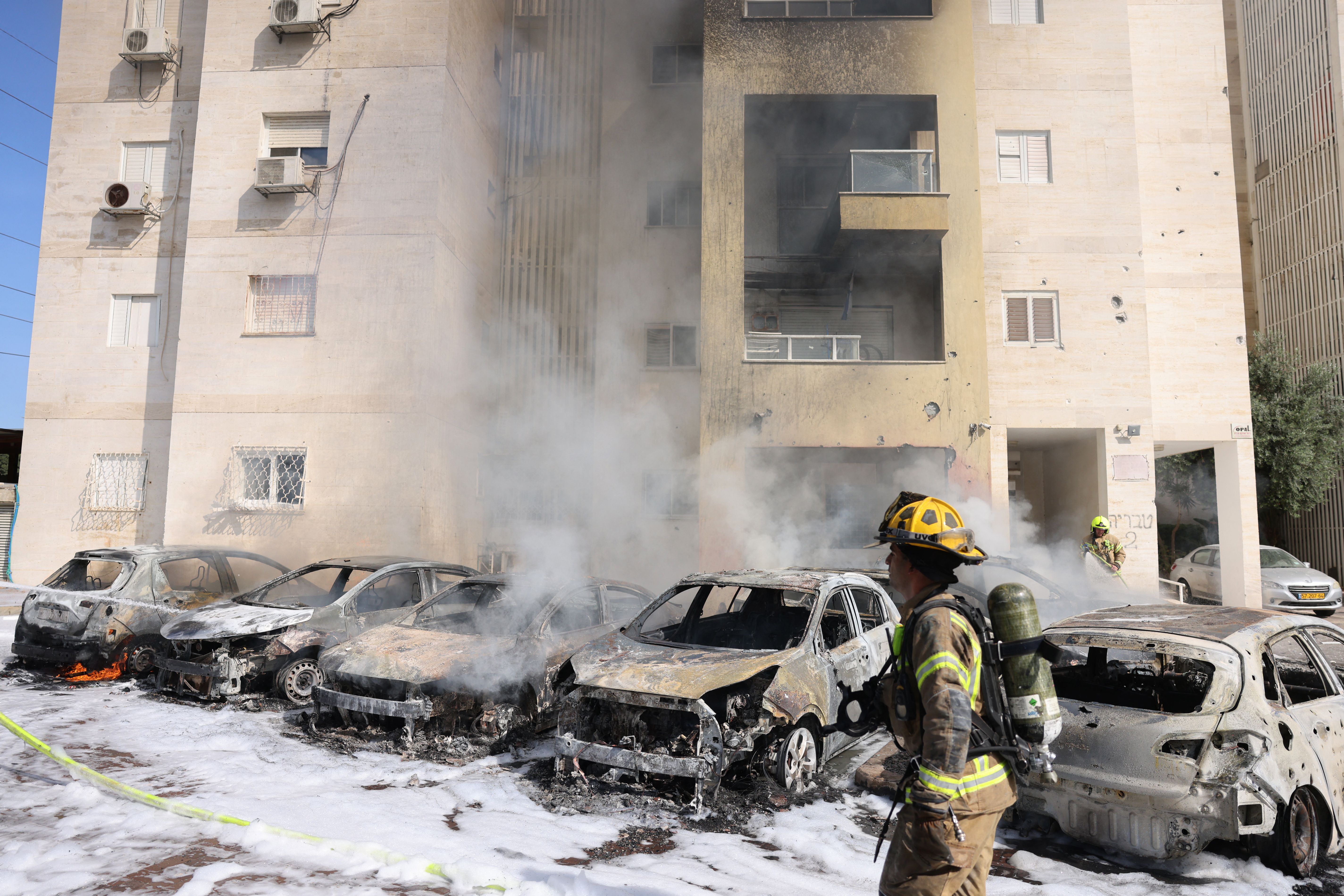 Israeli fire brigade teams douse the blaze in a parking lot outside a residential building following a rocket attack from the Gaza Strip in the southern Israeli city of Ashkelon, on October 7, 2023.
