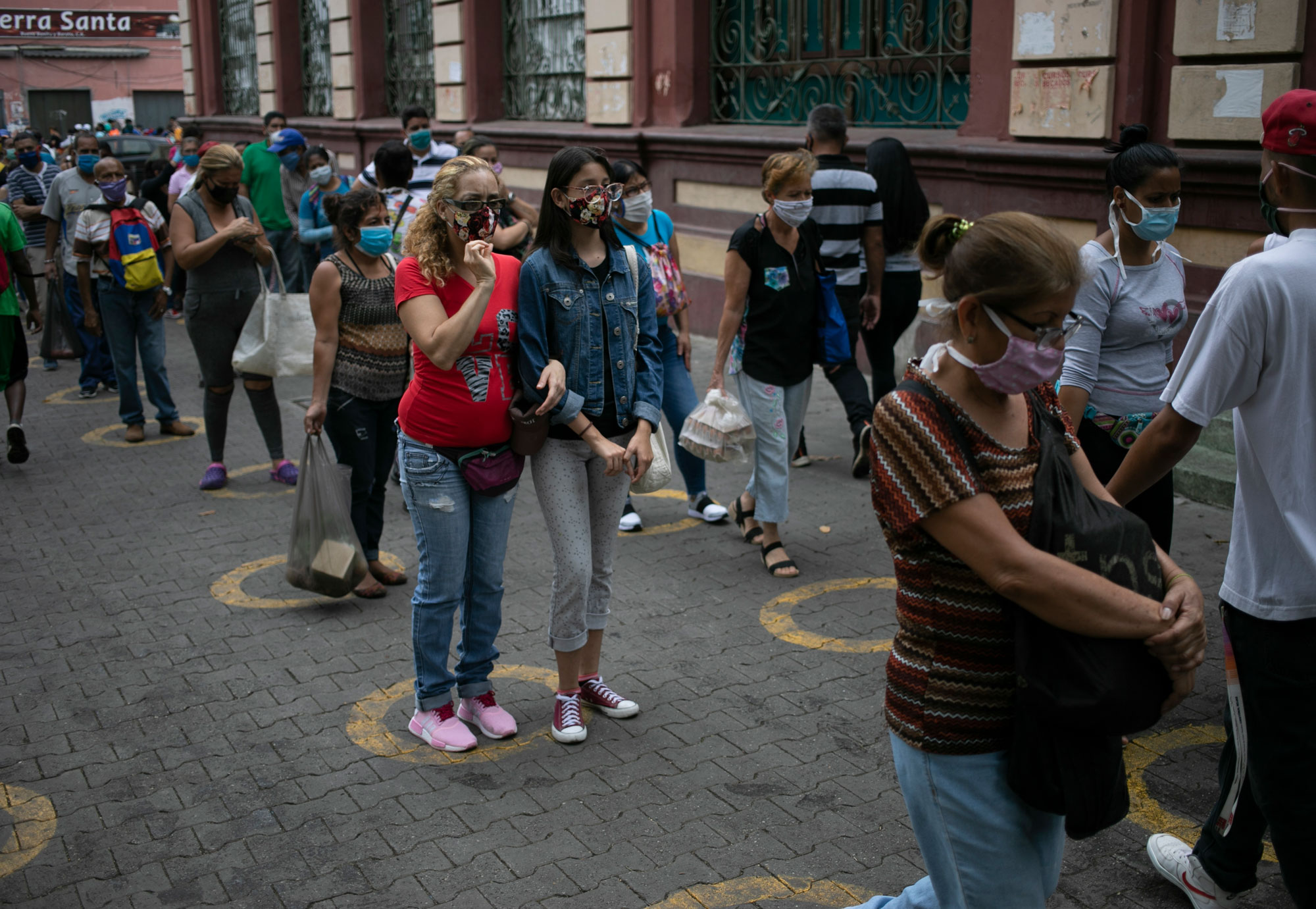 People stand over yellow circles painted on pavement that serve as visual cues to help shoppers adhere to social distancing before entering a popular market in the neighborhood of Catia in Caracas, Venezuela, on May 28.