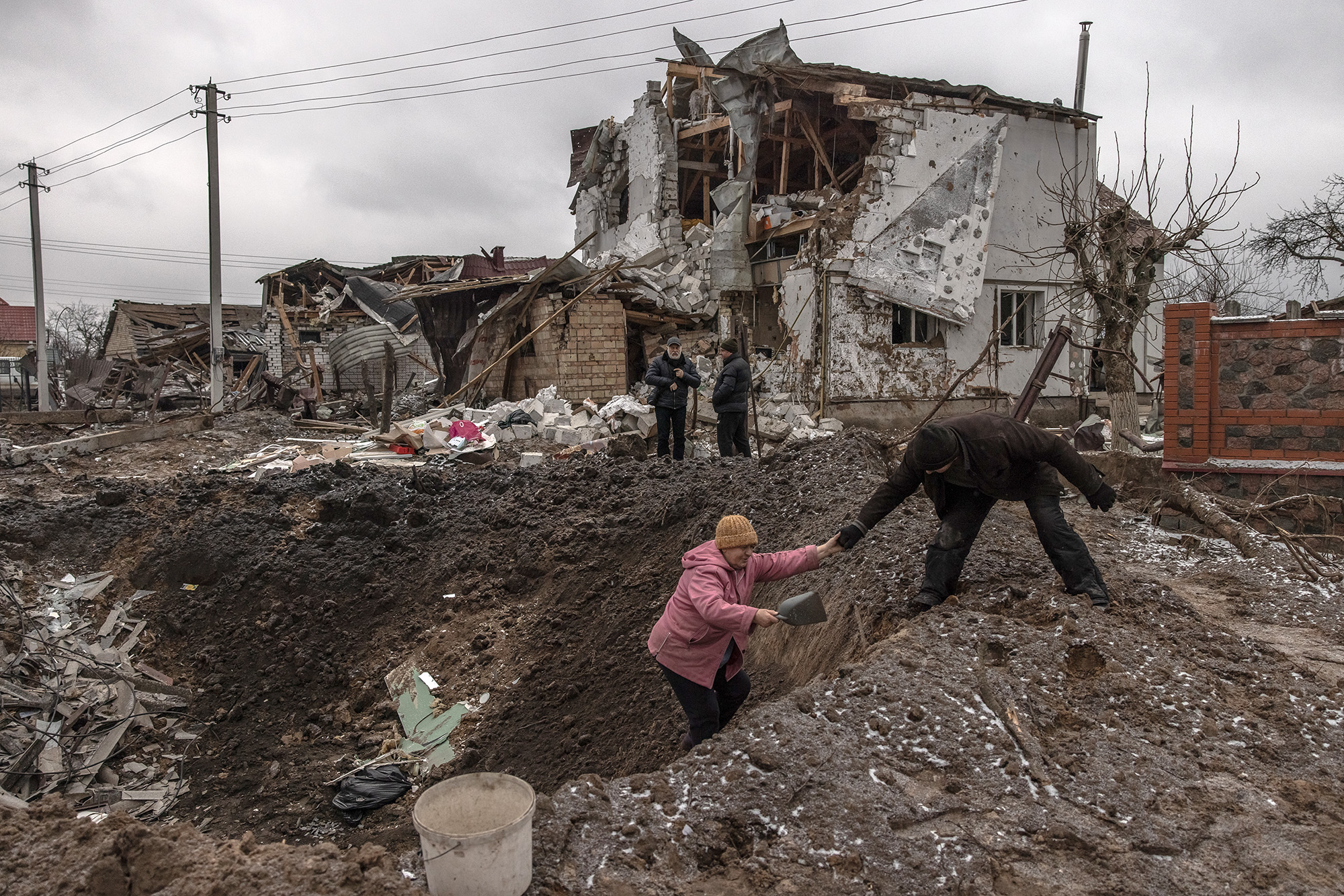 A man helps a woman to get out from a crater next to damaged residential buildings following a Russian missile attack on January 26, in Hlevakha, outside Kyiv, Ukraine. 
