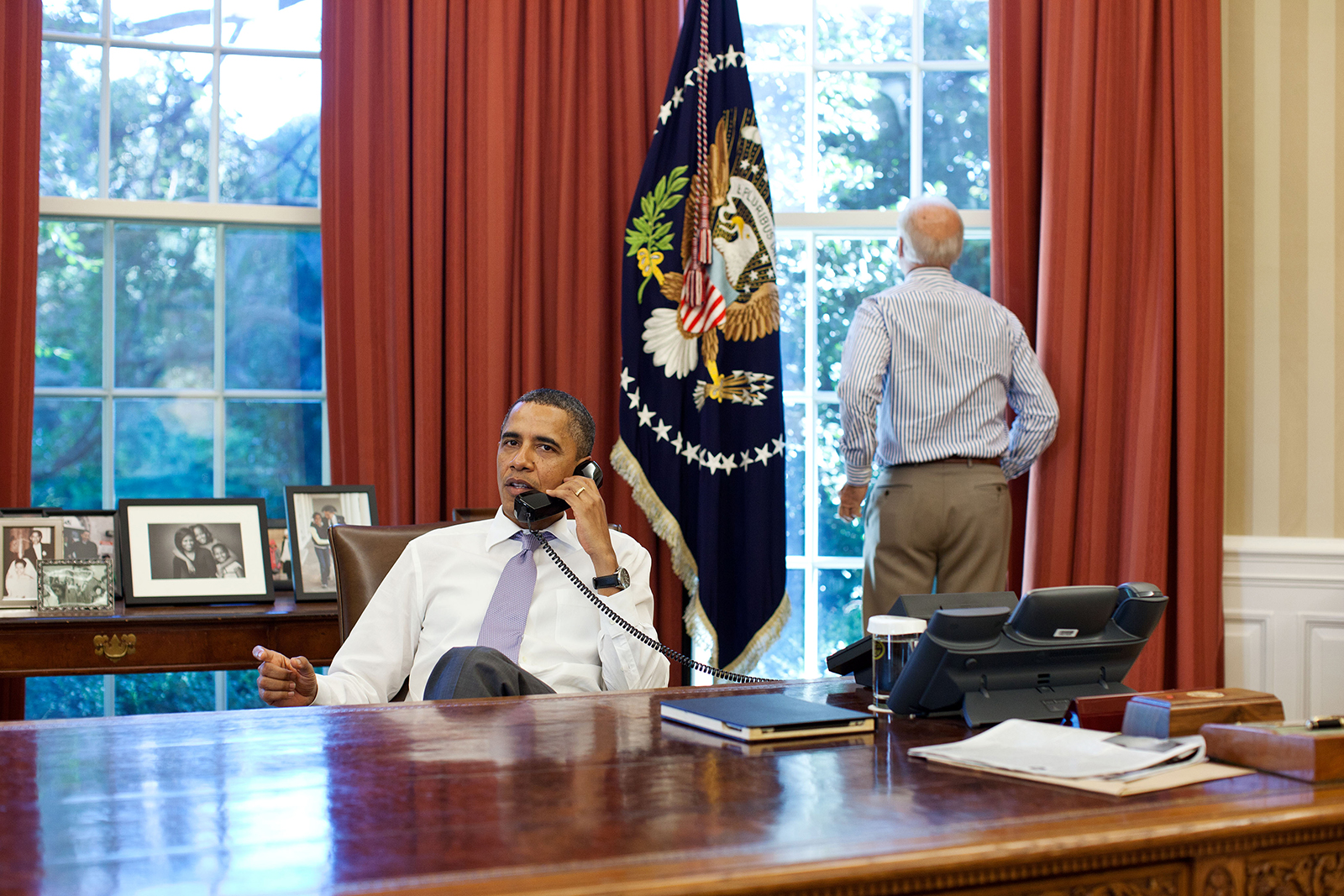 In this photo taken on July 31, 2011, then-Vice President Joe Biden (R) looks out the window as U.S. President Barack Obama talks on the phone with House Speaker John Boehner in the Oval Office to discuss ongoing efforts in the debt limit and deficit reduction talks in Washington, DC.