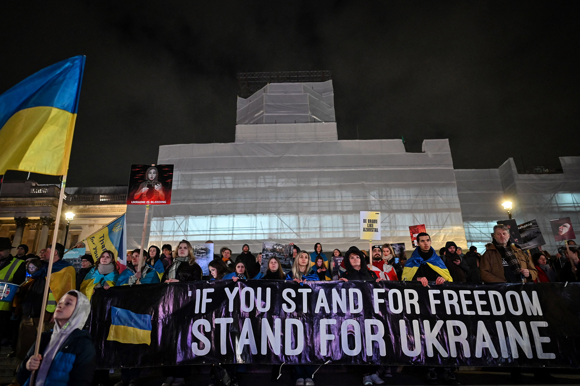 People wave Ukrainian flags and hold a banner as they attend a vigil in Trafalgar Square on February 23 to mark one year anniversary of Russias invasion of Ukraine.