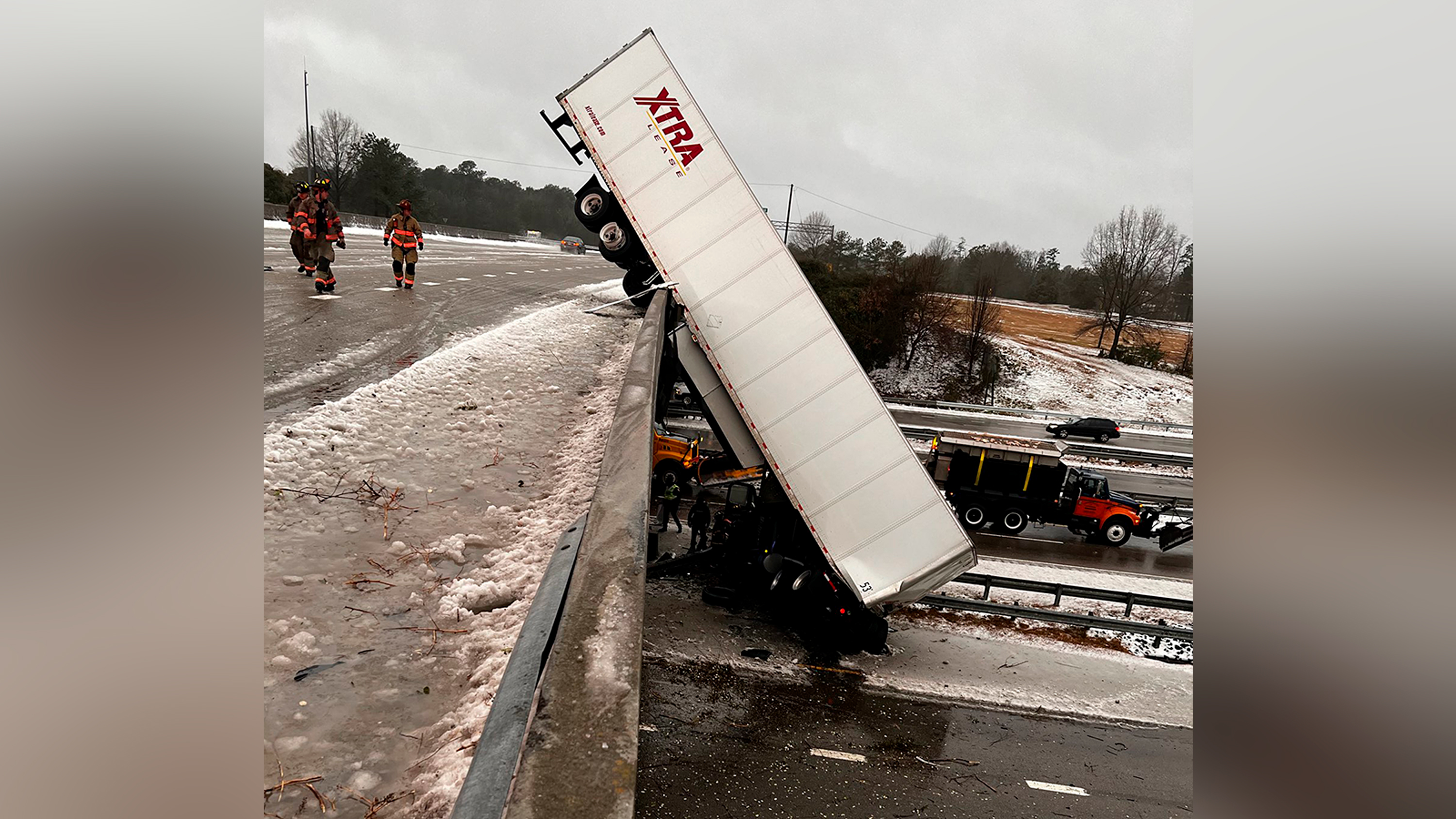 In this photo provided by the Durham Police Department, a truck hangs from the highway N.C. 147 overpass after its cab apparently slid off the highway during winter weather, Sunday, January 16, in Durham, N.C. The cab of the truck appeared to have landed upright on Highway 15-501 below, while the trailer was in a vertical position, from the bridge to the highway below, causing road closures. 