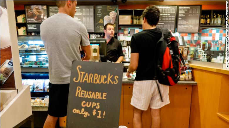 Interior of Starbucks Coffee with customers standing at the counter behind reusable cups sign.