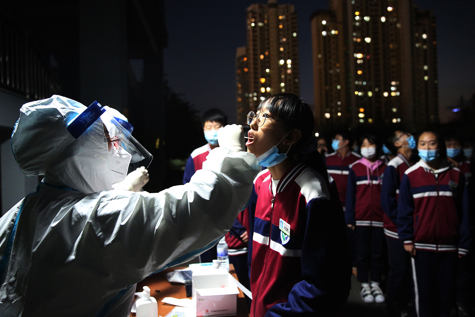 This photo taken on October 12 shows a health worker taking a swab from a middle school student to be tested for Covid-19, as part of a mass testing program following a new coronavirus outbreak in Qingdao, in China's eastern Shandong province. 