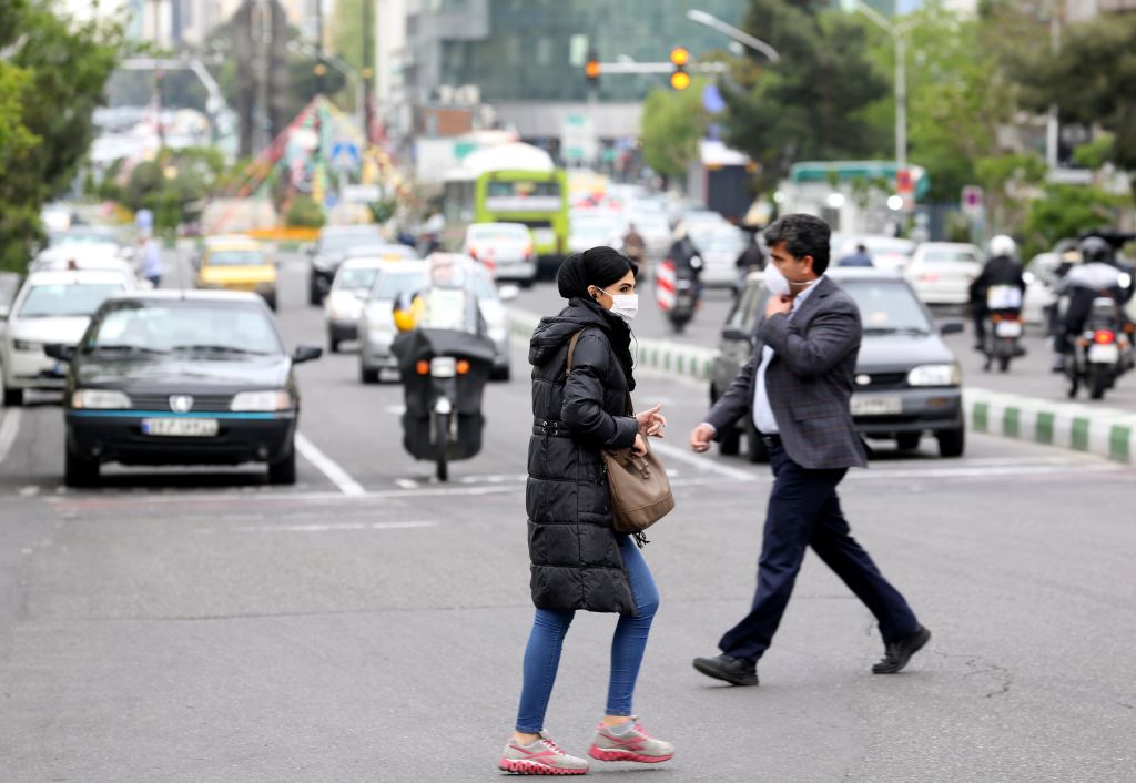 Iranians wearing protective masks cross a main road in Tehran on April 13.