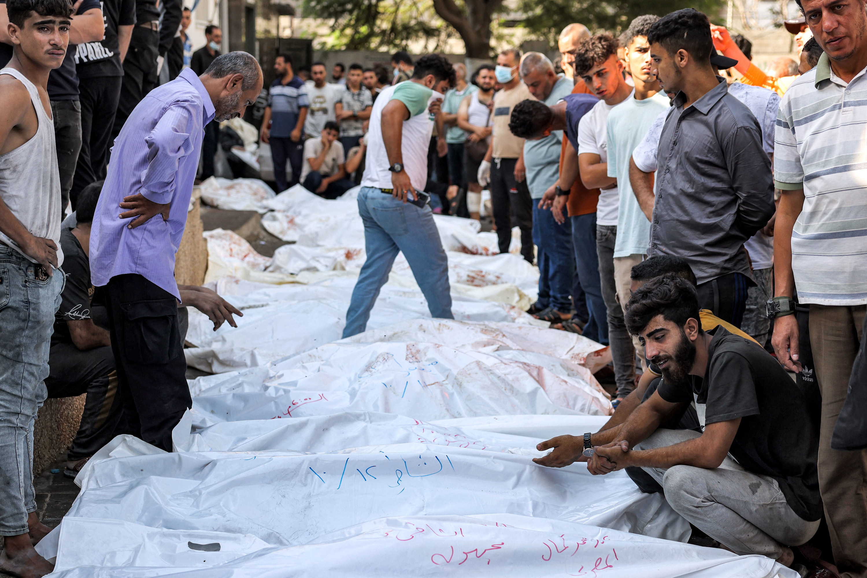 People stand by the bodies of victims of Israeli air strikes outside the morgue of al-Shifa hospital in Gaza City on October 12, 2023.