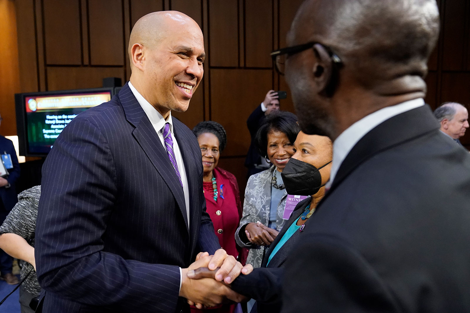 Sen. Cory Booker shakes hands with Johnny Brown, father of Supreme Court nominee Judge Ketanji Brown Jackson, during a break in her confirmation hearing Tuesday evening.