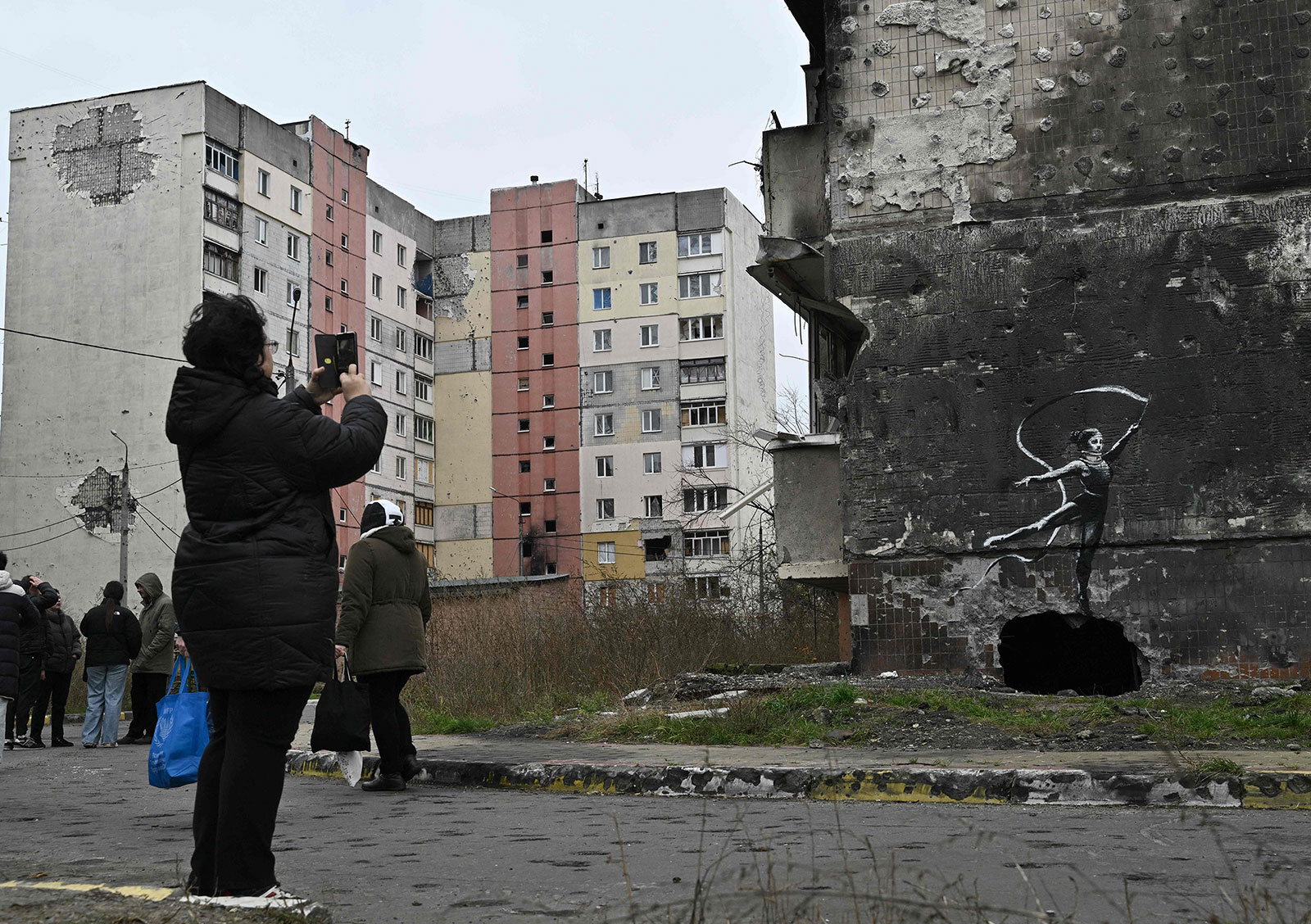 A local resident takes a picture of the artwork on the wall of a destroyed residential building, in Irpin, Ukraine, on November 12, 2022.