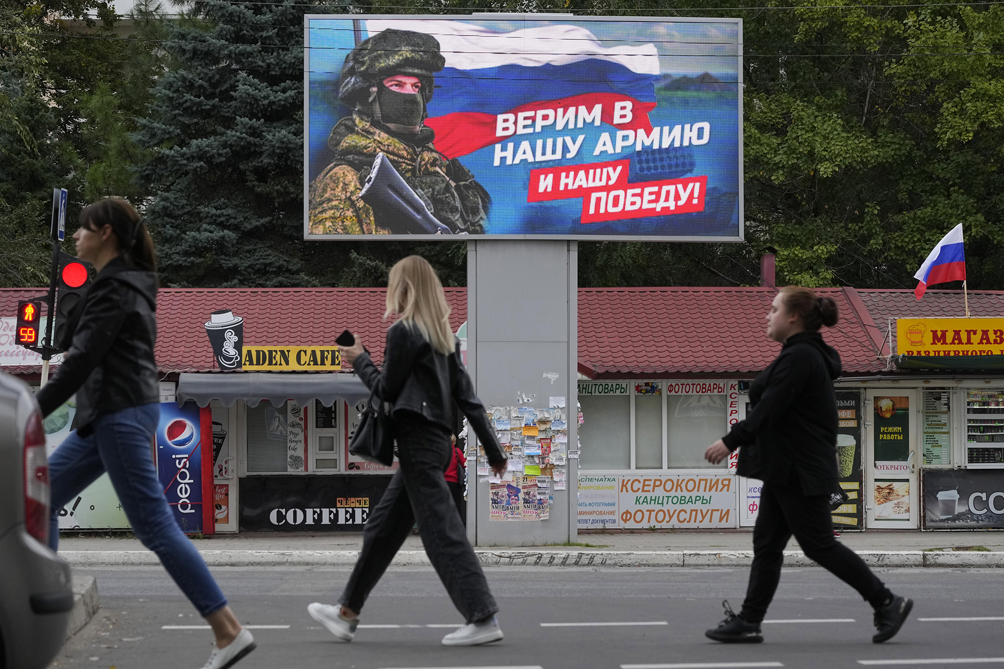 People walk past a billboard displaying a soldier and a Russian flag and reading 'We believe in our army and our victory' in Luhansk, eastern Ukraine, on September 27.