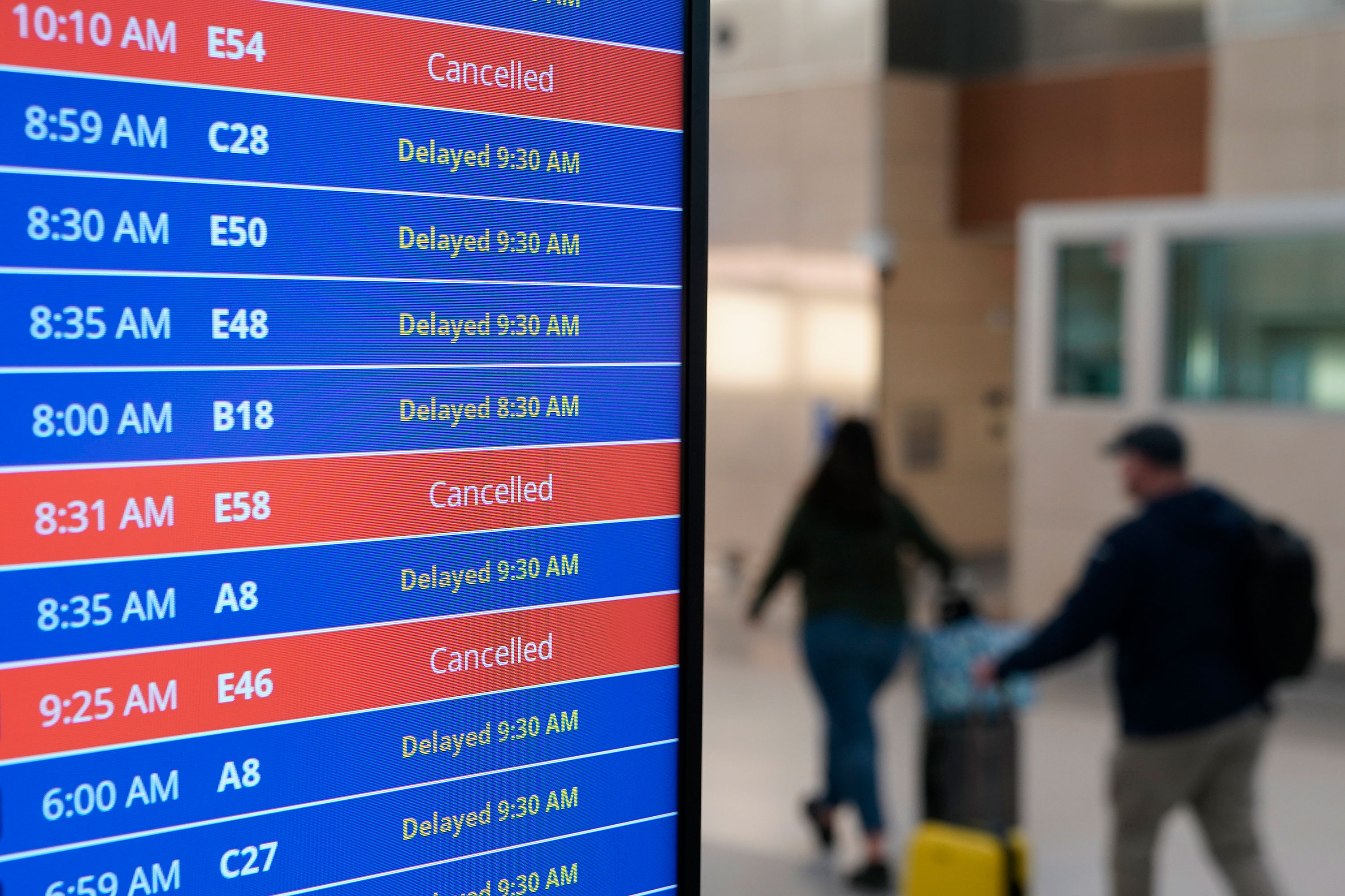 Travelers walk past a video board showing flight delays and cancellations at Ronald Reagan Washington National Airport on Wednesday.