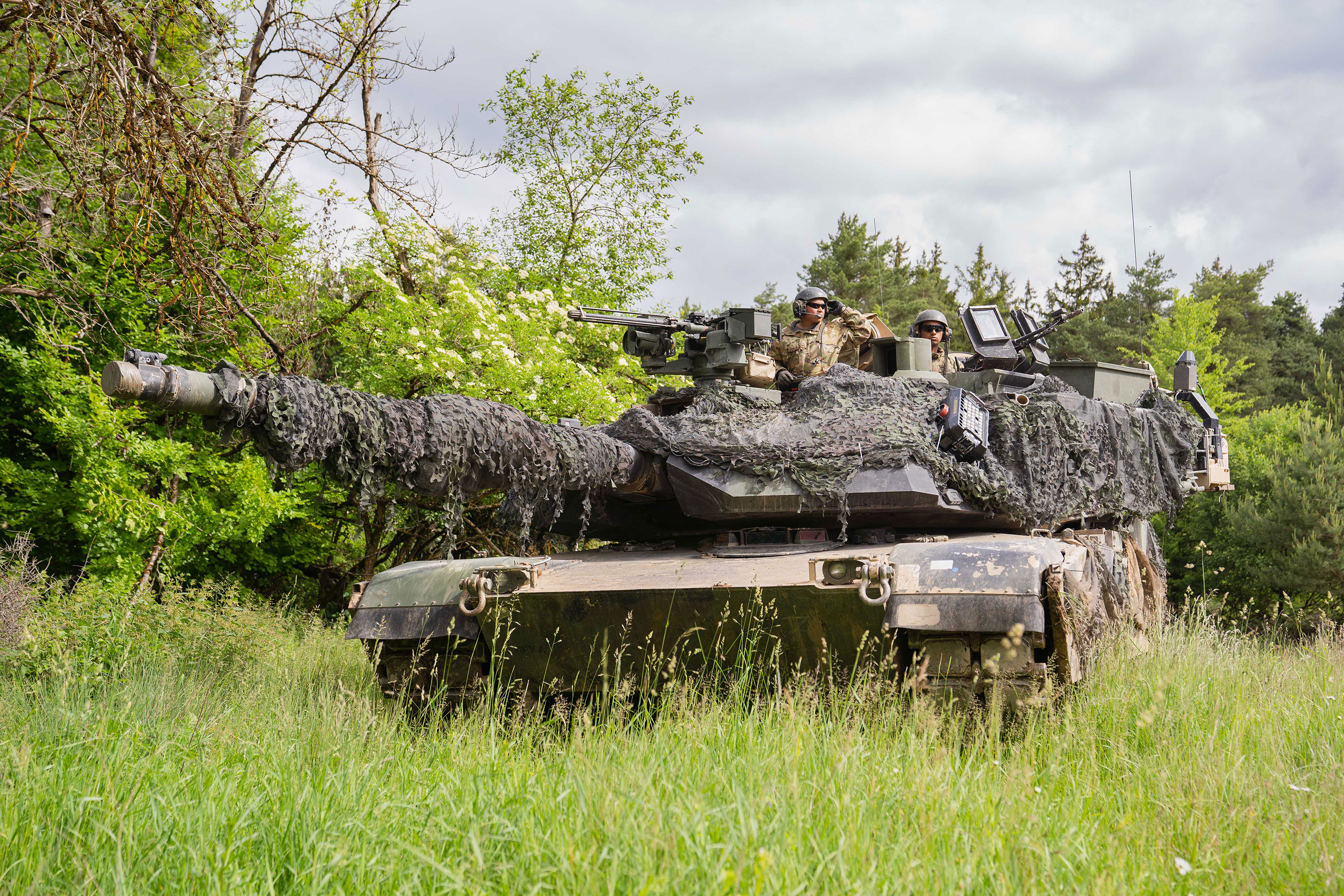 U.S. soldiers stand next to an M1 Abrams tank in a wooded area during a multinational exercise in June 2022 in Hohenfels, Germany.