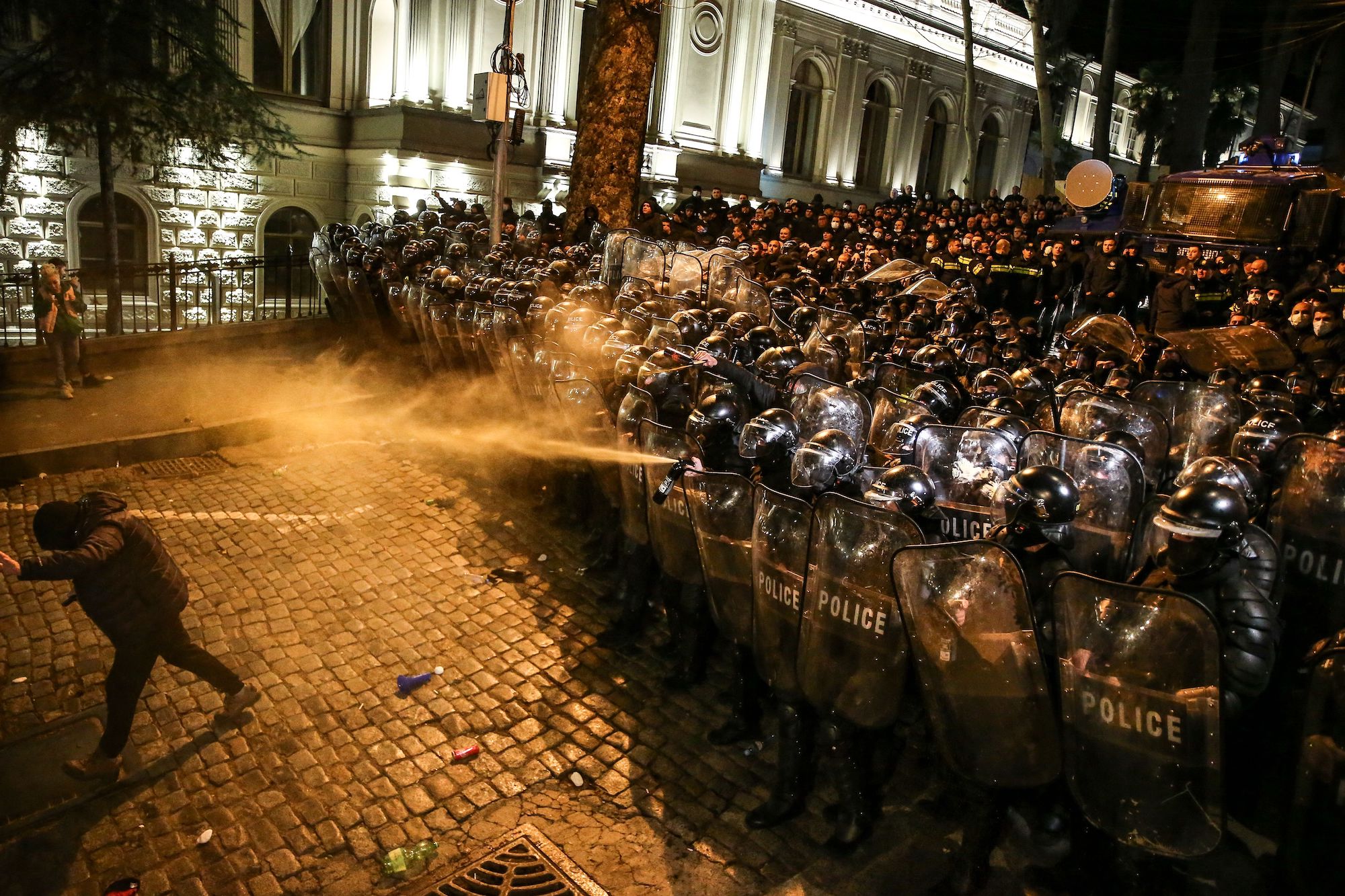 Riot police spray tear gas towards a protester as they form a cordon.
