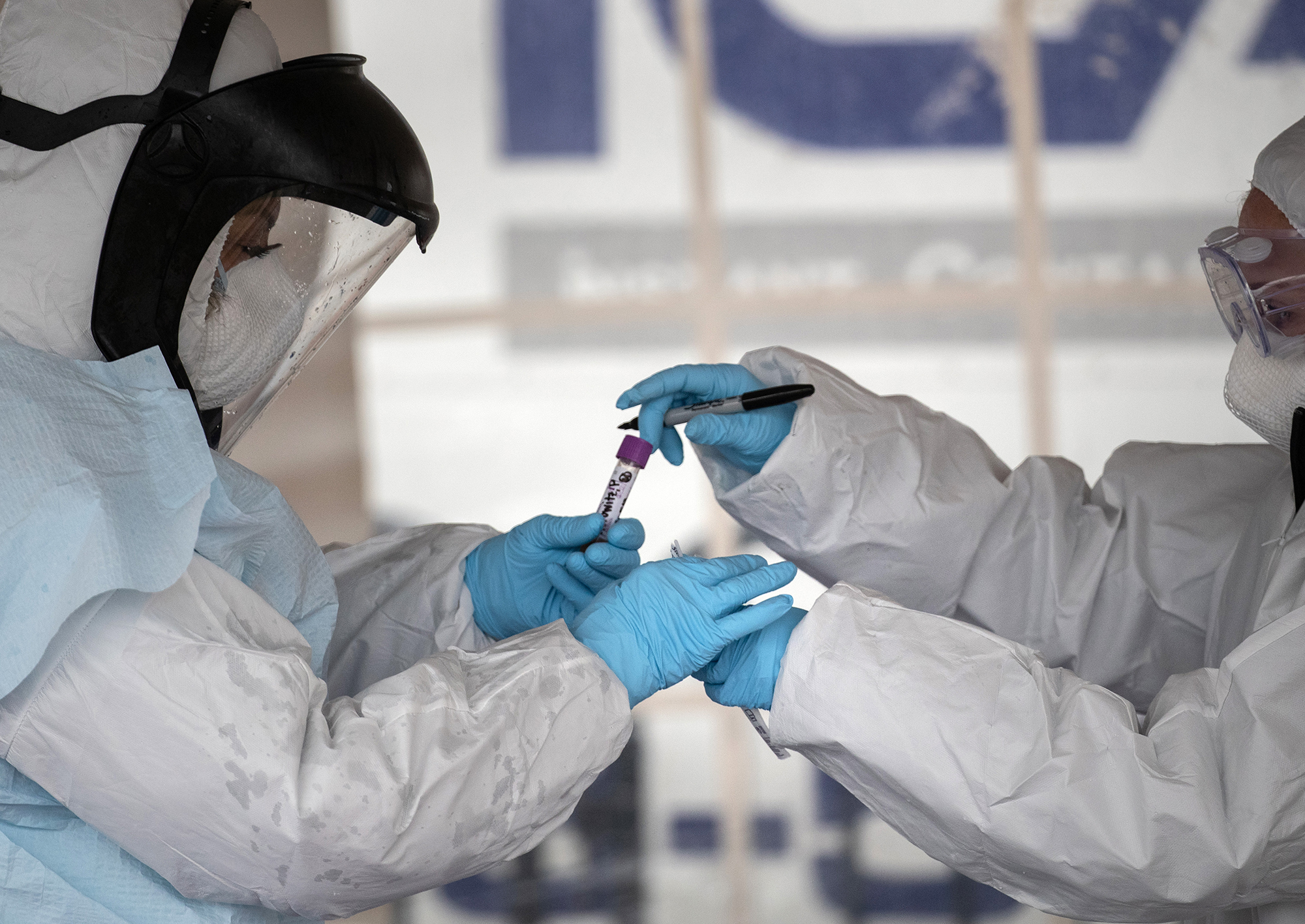 Health workers dressed in personal protective equipment handle a coronavirus test at a drive-thru testing station at Cummings Park on March 23, in Stamford, Connecticut.