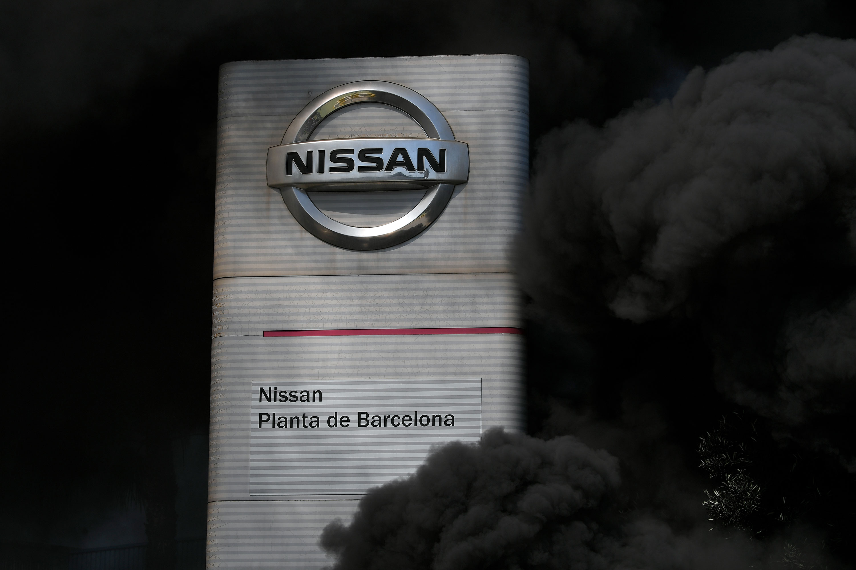 The logo of Nissan is covered by smoke columns as employees burn tires in front of the Japanese cars manufacturer's plant in Barcelona on May 28 to protest the factory closure. 