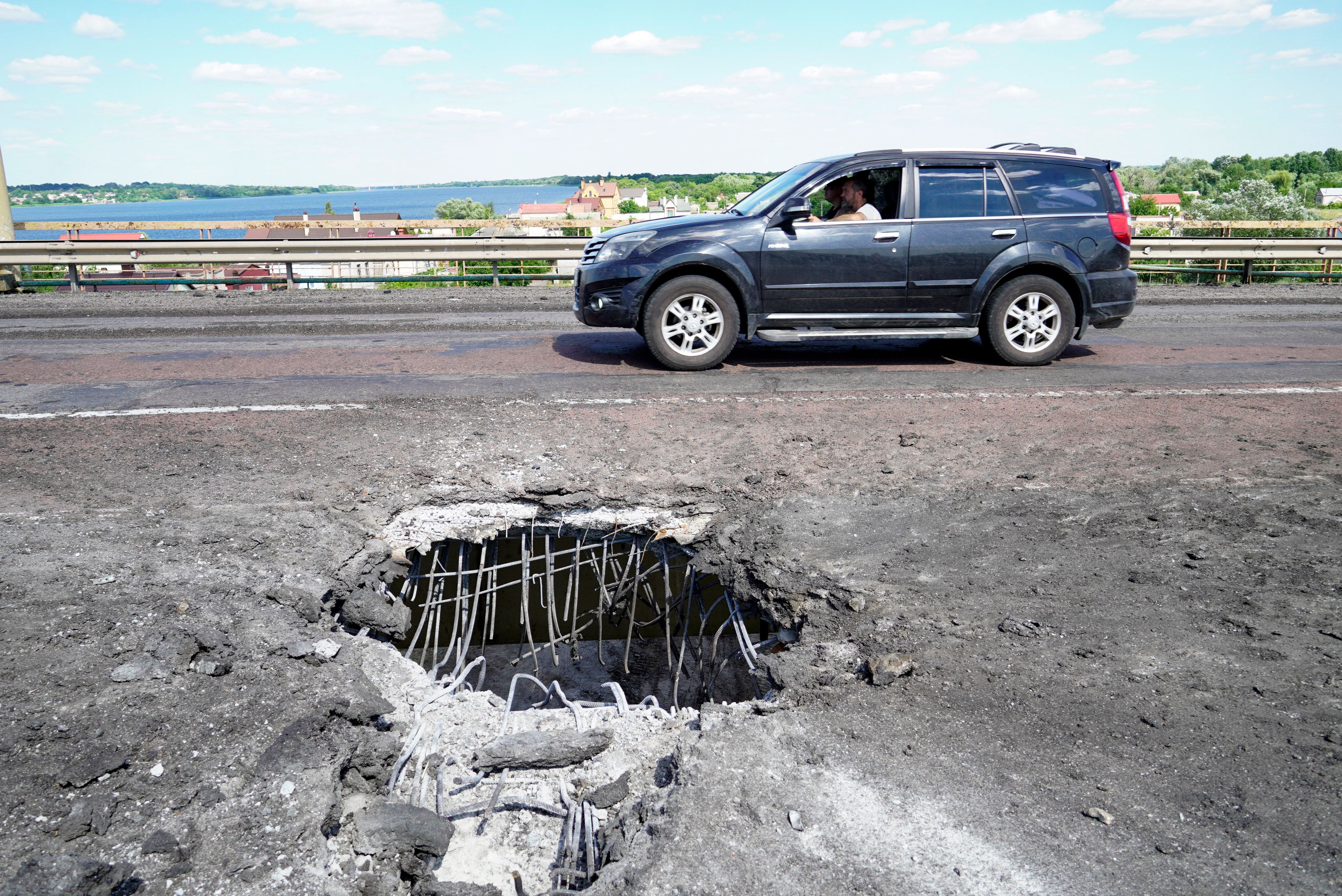A picture taken on July 21 shows a car moving past a crater on a bridge across the Dnipro river, near Kherson, caused by a Ukrainian rocket strike.