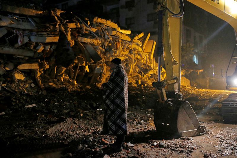 A man stands in front of a collapsed building in Osmaniye, Turkey.