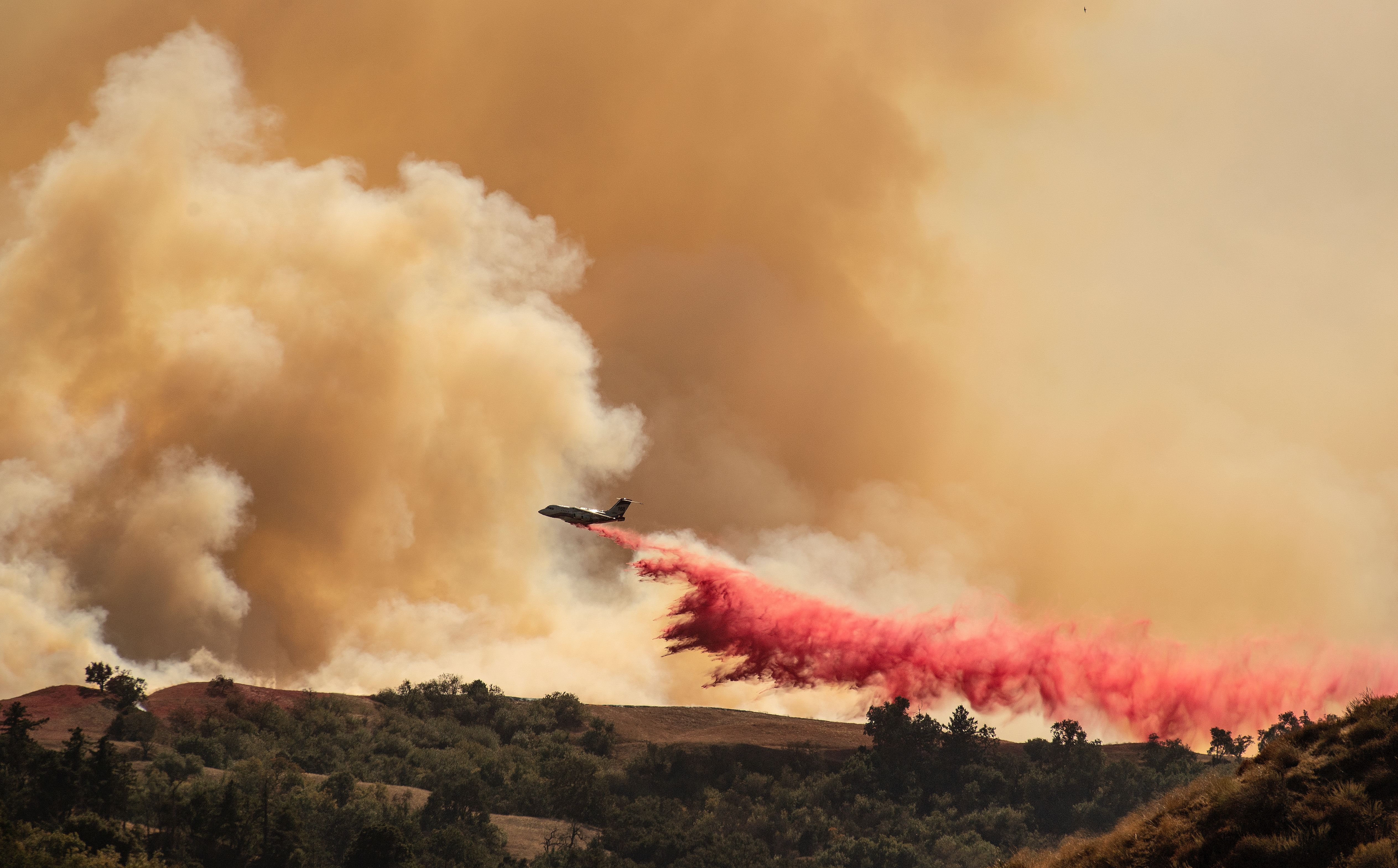 An aircraft helps fight the Saddleridge Fire by dropping fire retardant along a ridge in Newhall, California on Oct. 11, 2019. 