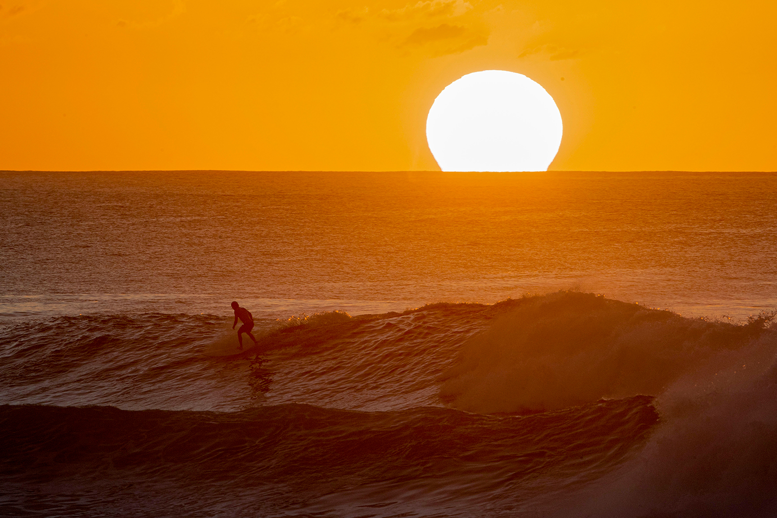 A surfer rides a wave as the sun sets on the horizon on the north shore of Oahu in Hawaii on January 28.