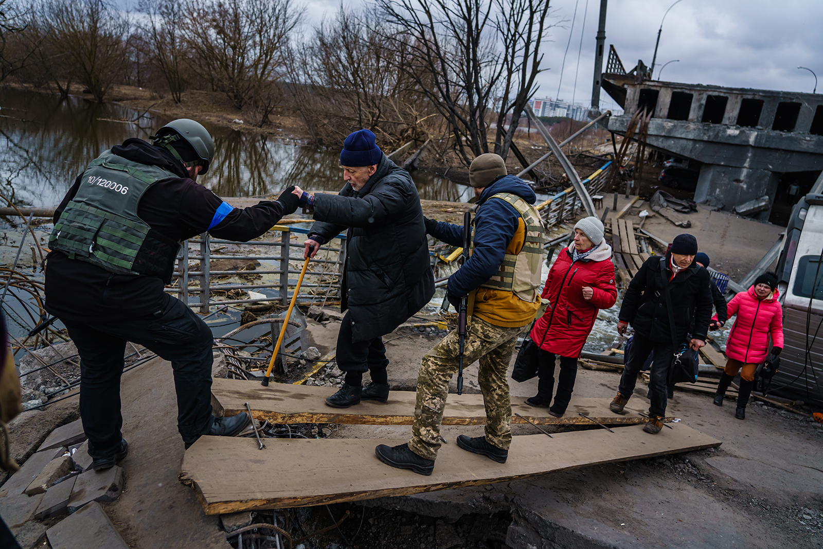 Ukrainian soldiers help civilians cross a makeshift walkway over a destroyed bridge to evacuate out of Irpin, Ukraine, on March 13.