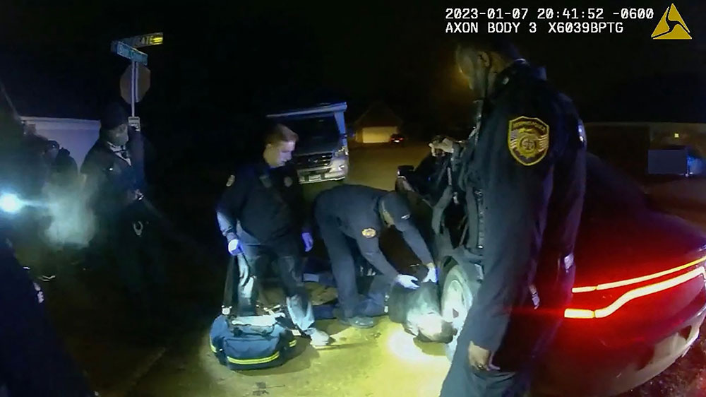 Paramedics check on Tyre Nichols as he lays handcuffed on the ground surrounded by police officers 