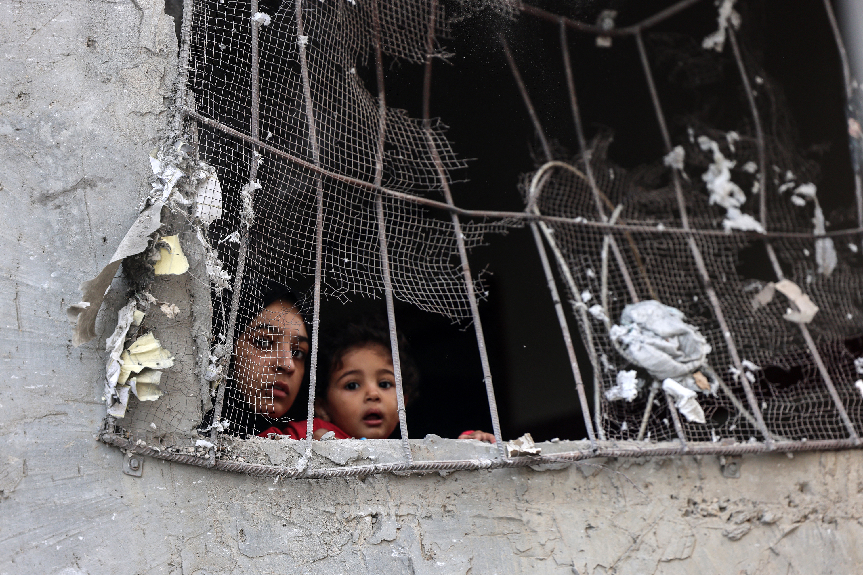 A woman and a child look out from the window of a damaged building following an Israeli bombing of Rafah, Gaza, on November 2023. 