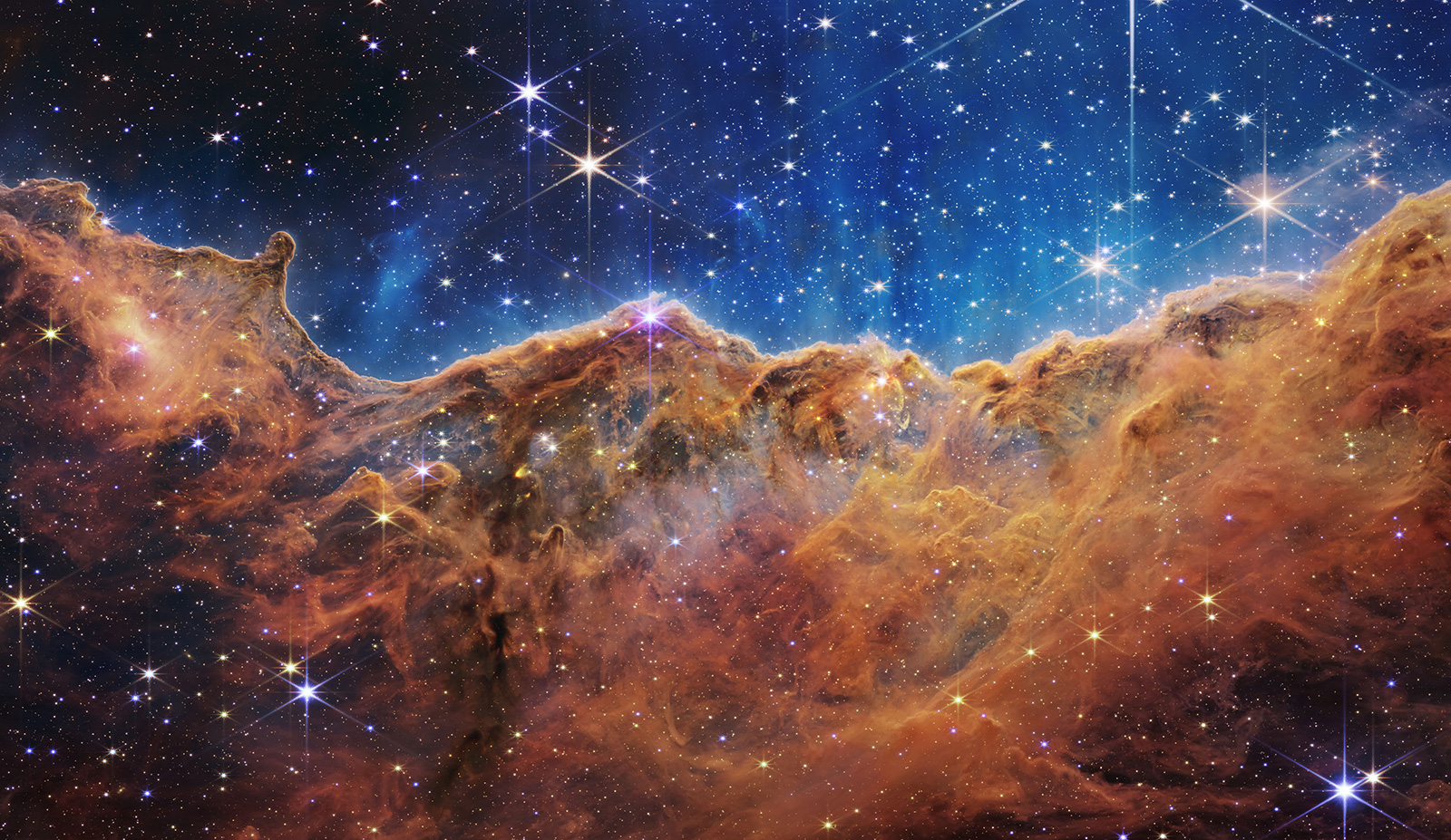 This landscape of “mountains” and “valleys” speckled with glittering stars is actually the edge of a nearby, young, star-forming region called NGC 3324 in the Carina Nebula. Captured in infrared light by NASA’s new James Webb Space Telescope, this image reveals for the first time previously invisible areas of star birth. 