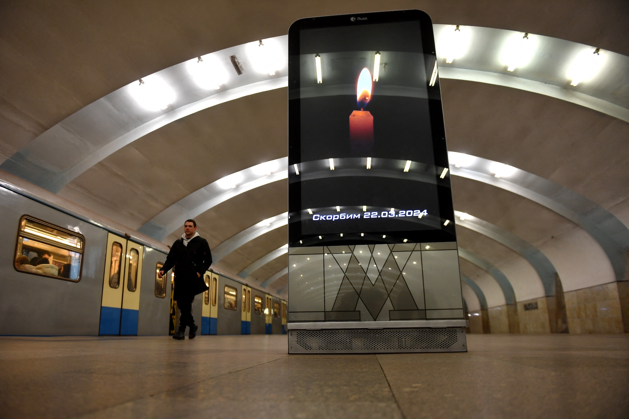 Một người đàn ông đi ngang qua màn hình quảng cáo hiển thị hình ảnh một ngọn nến được thắp sáng trong tàu điện ngầm ở Moscow vào Chủ nhật.