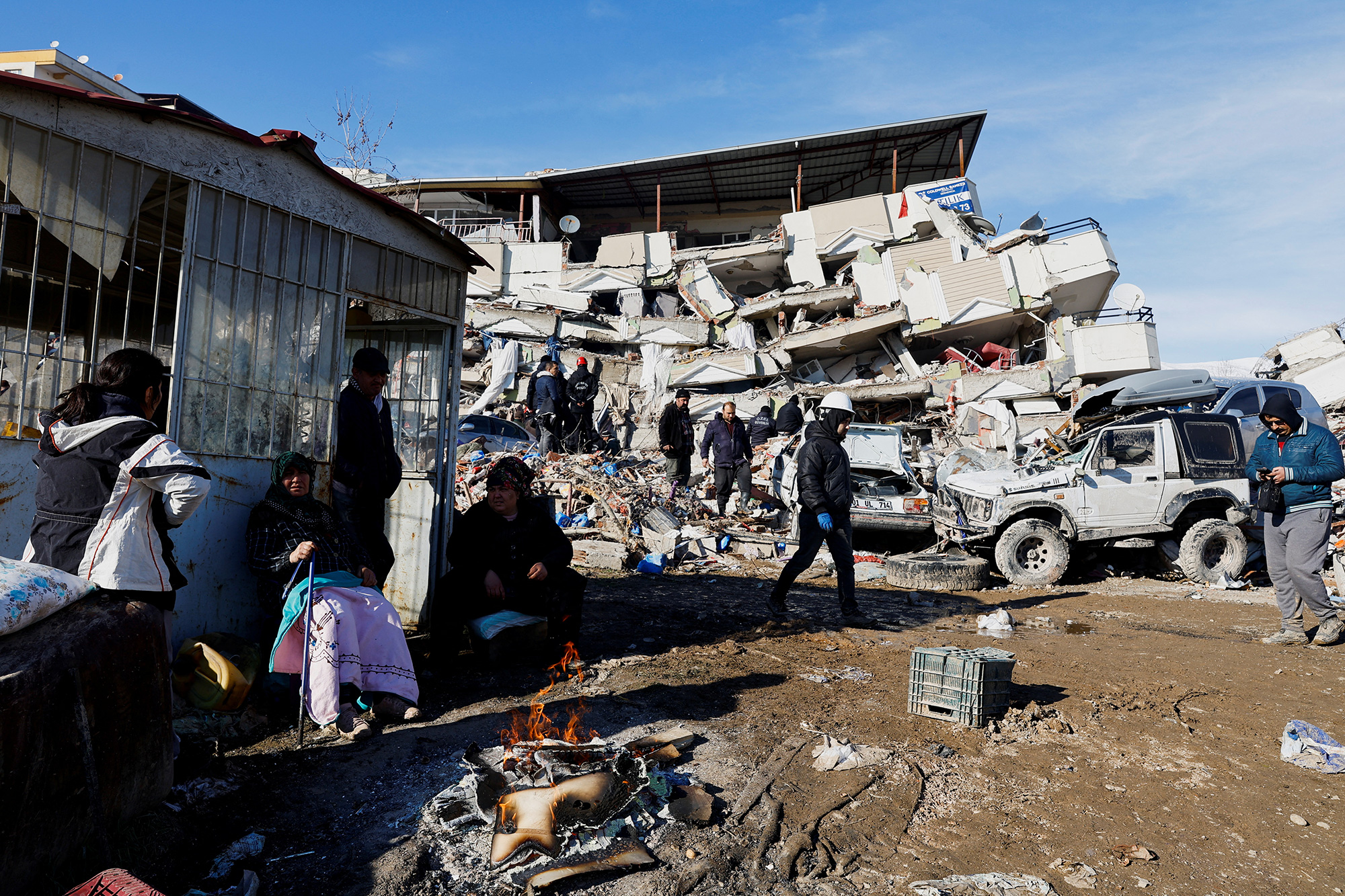 People sit next to a fire near the site of a collapsed building in Kahramanmaras, Turkey, on February 7.