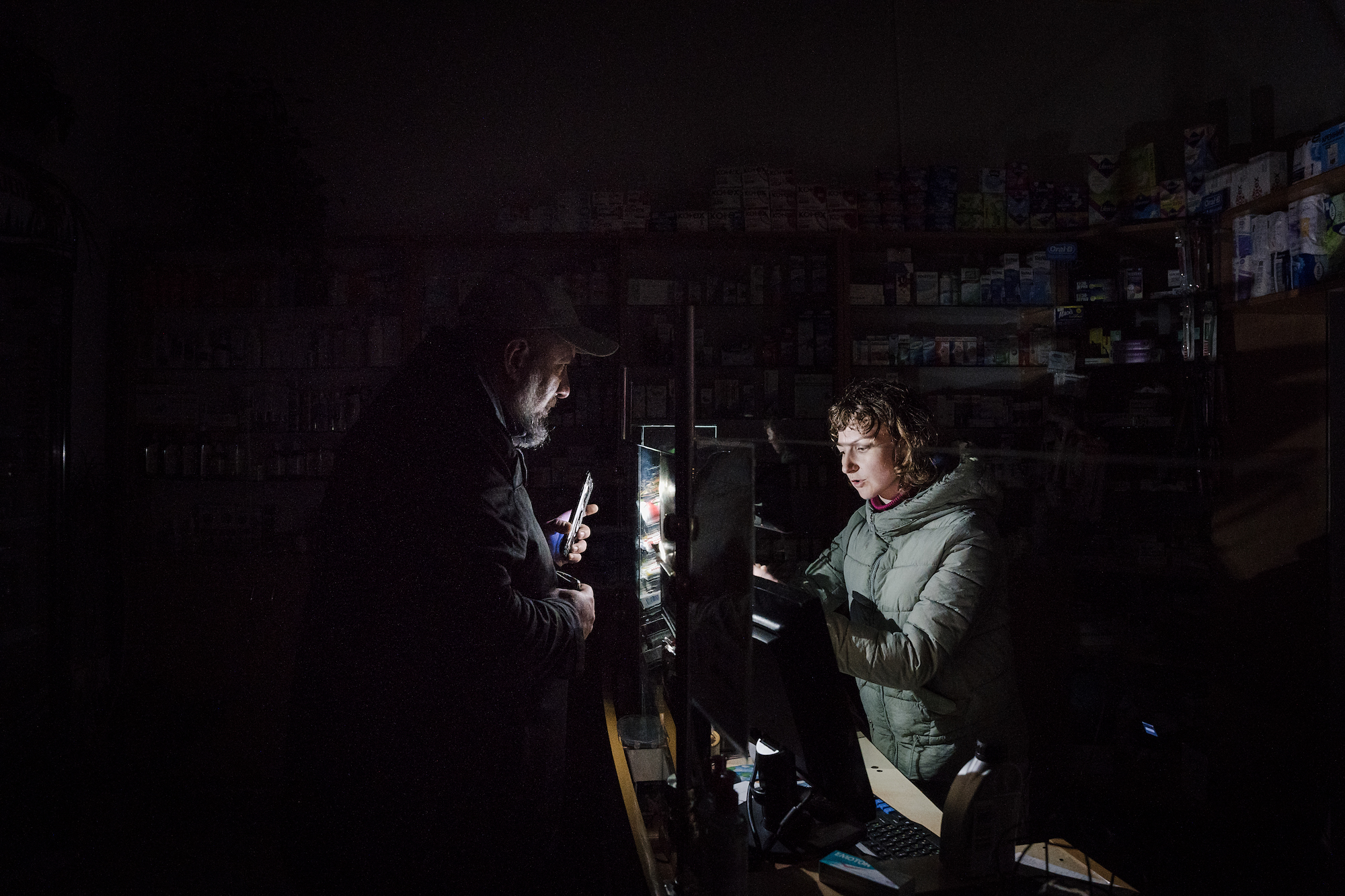 A man helps a pharmacist find a product with his cellphone flashlight in Lviv on Wednesday. 