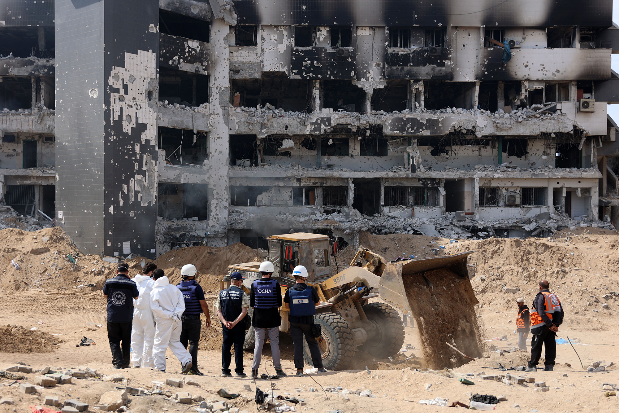 A United Nations team looks on as Gaza Civil Defense recover human remains the grounds of Al-Shifa hospital, in Gaza, on April 8, 2024.