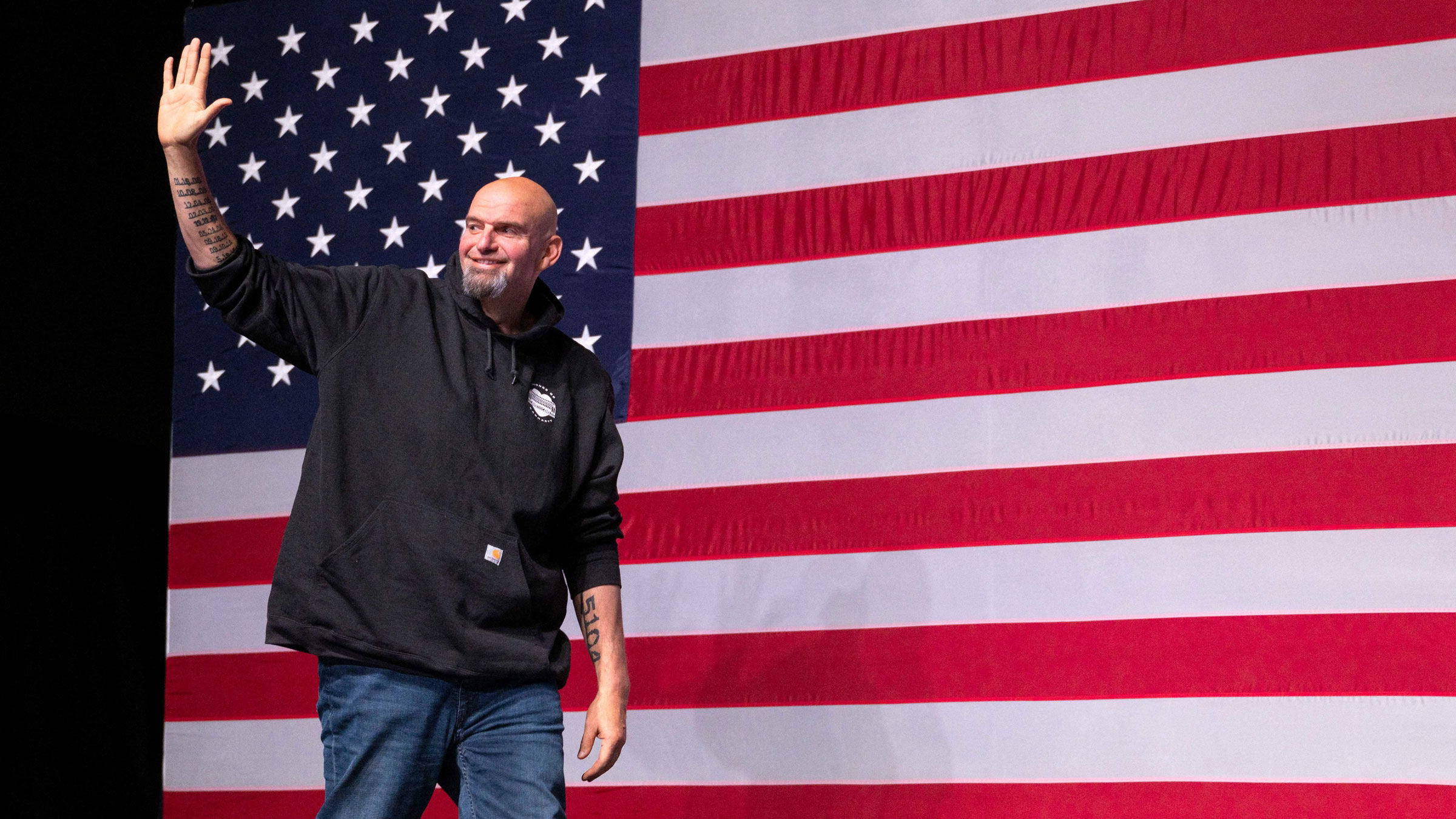 John Fetterman waves as he walks on stage at a watch party in Pittsburgh.